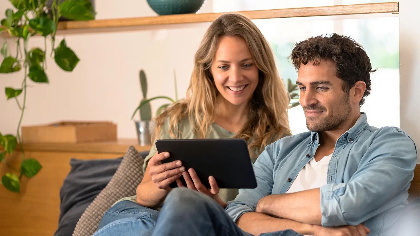 Ein Paar sitzt auf der Couch und informiert sich im Internet mit einem Tablet