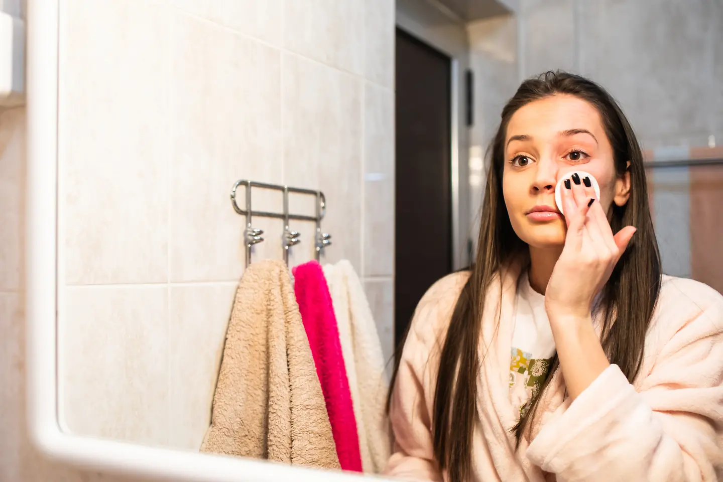Eine junge Frau schminkt sich vor ihrem Badezimmerspiegel ab um einem Gerstenkorn vorzubeugen