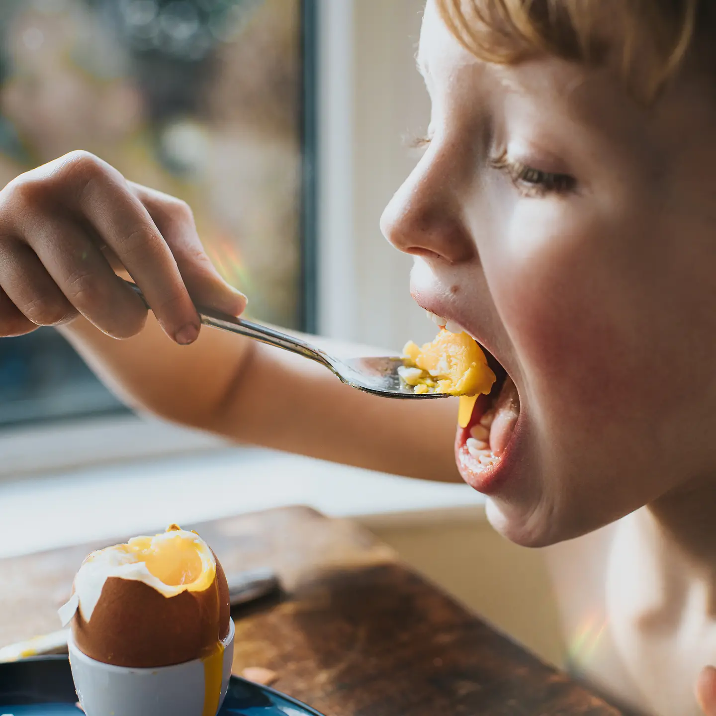 Ein Junge löffelt Eigelb aus einem hartgekochten Ei