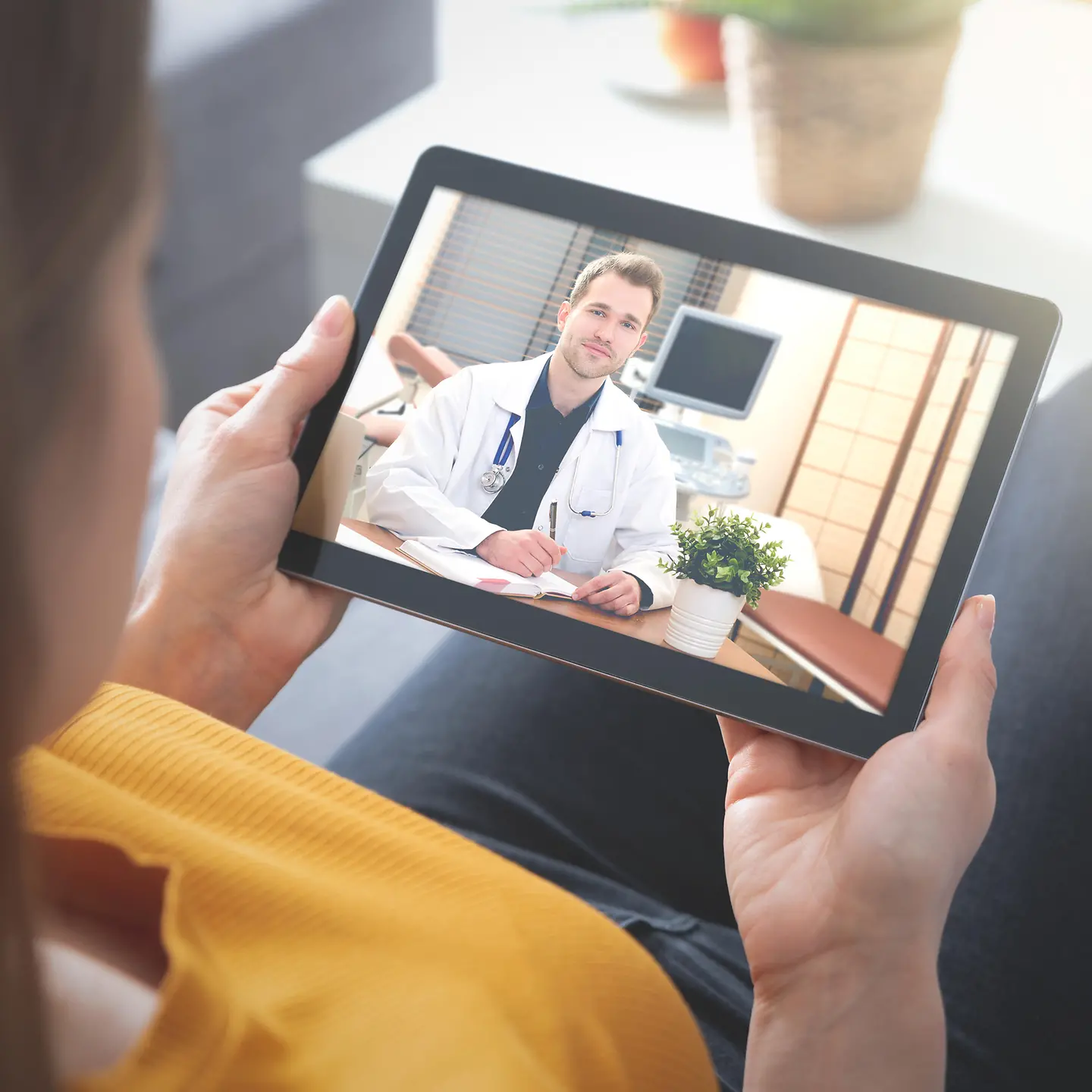 Eine Frau hält ein Tablet in den Händen und spricht über Video mit ihrem Arzt.