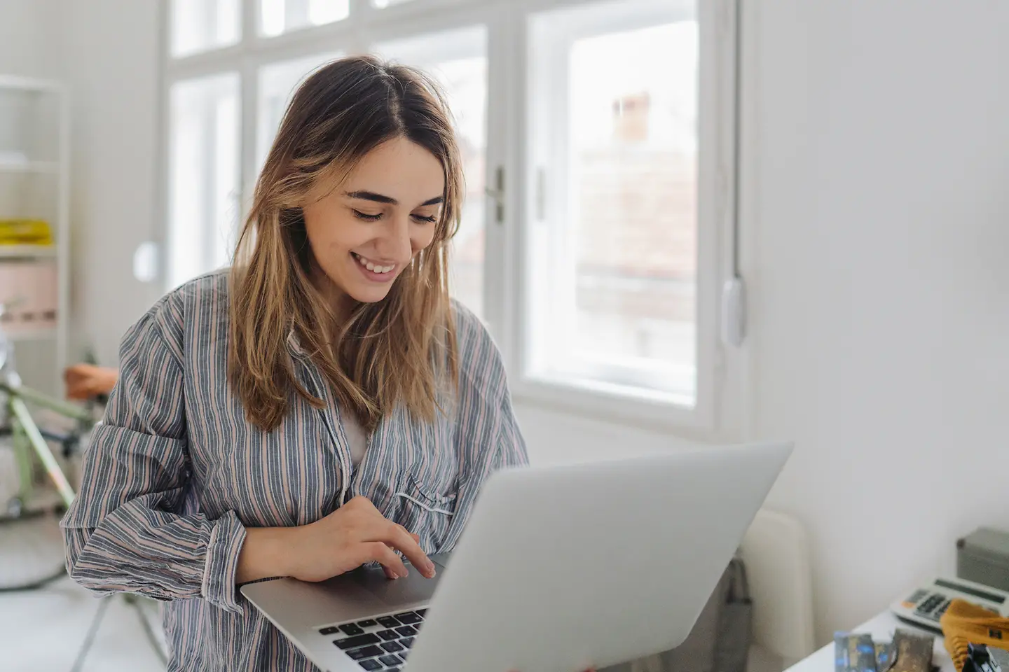 Junge Frau schaut auf den Bildschirm ihres Laptops im Arm und lächelt