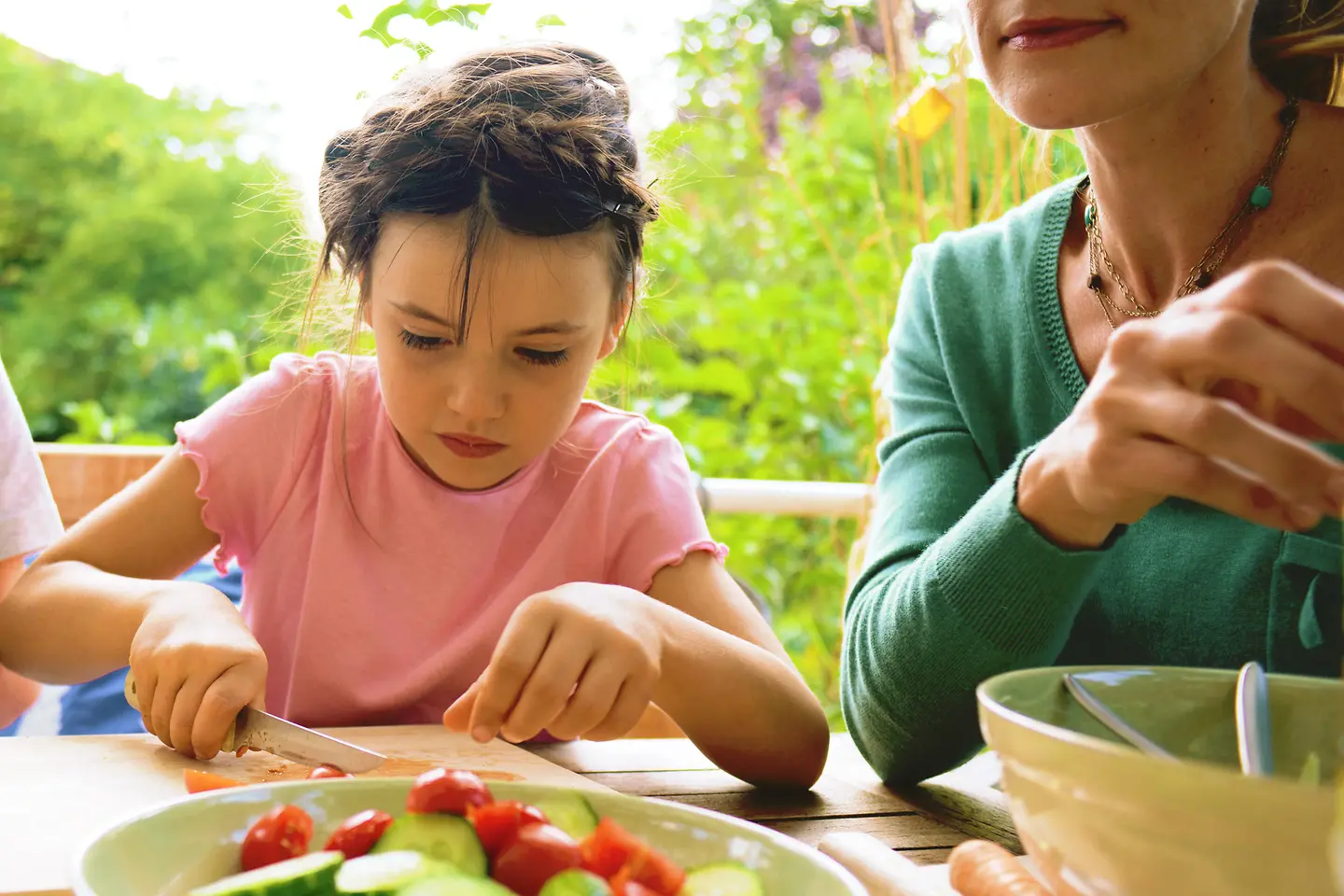 Eine Mutter und zwei Kinder sitzen an einem Tisch und schneiden Gemüse.