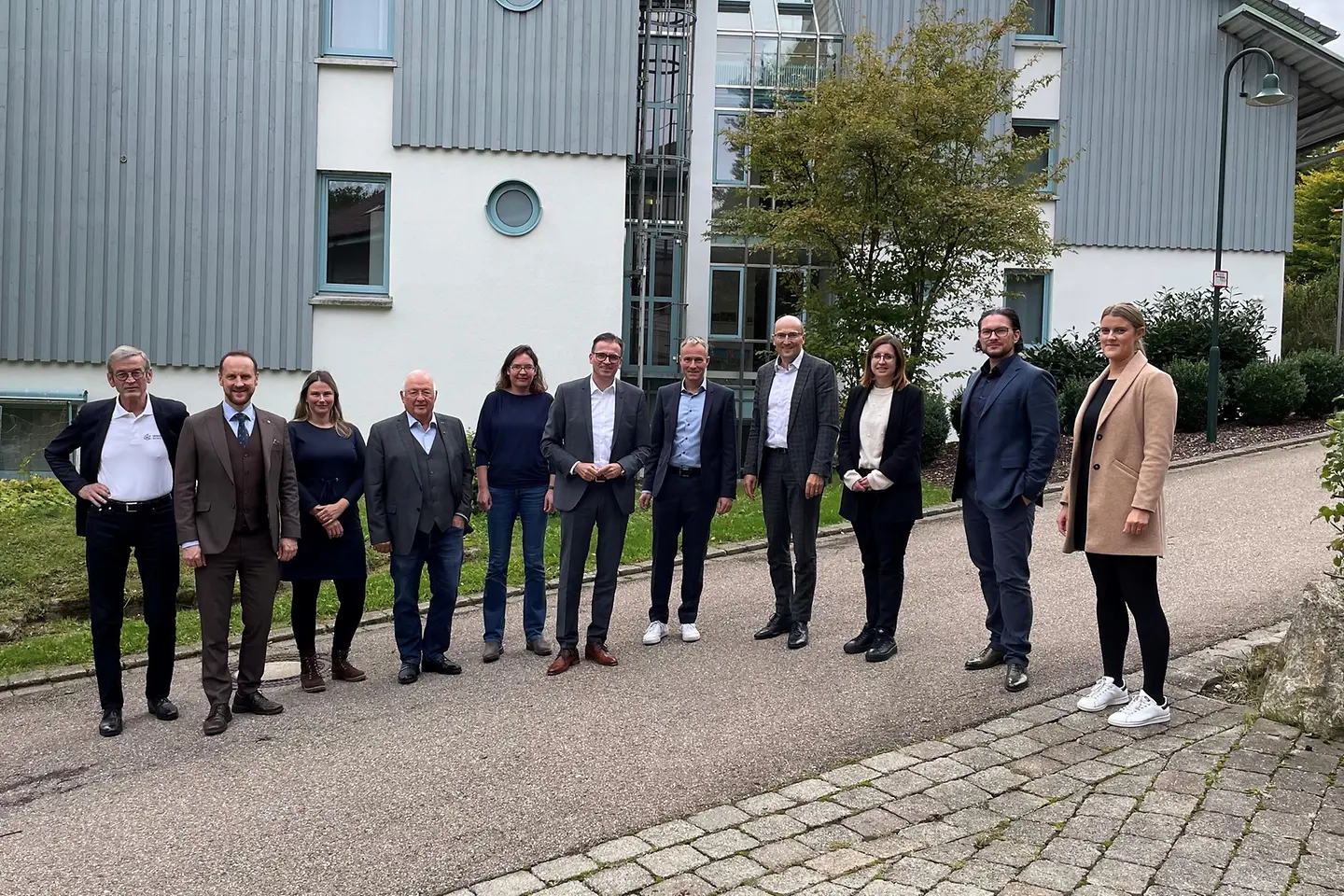 7 Männer und 4 Frauen stehen nebeneinander vor einem Gebäude