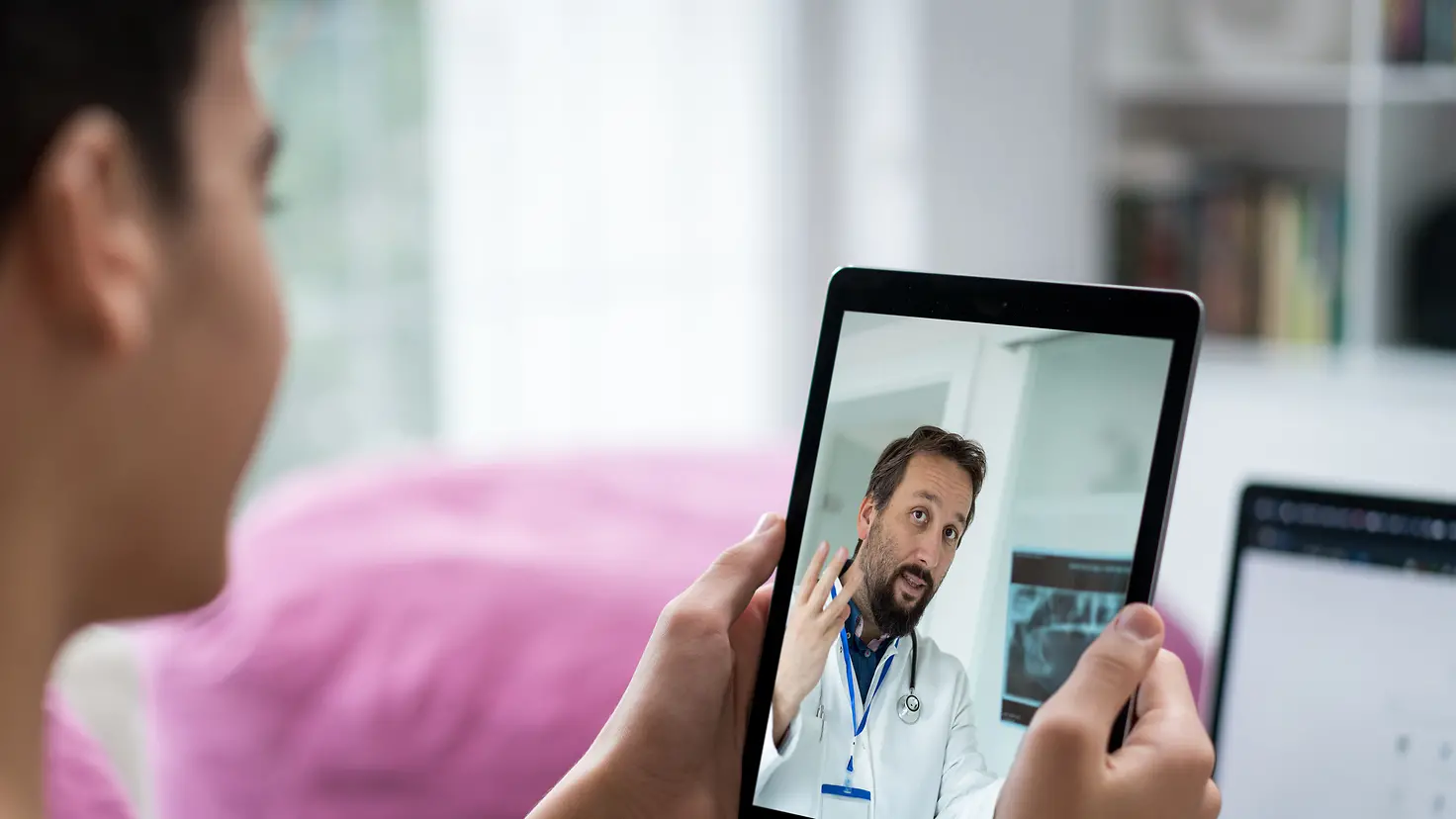 Ein Frau hält ein Tablet in der Hand, auf dem ein Arzt zu sehen ist.