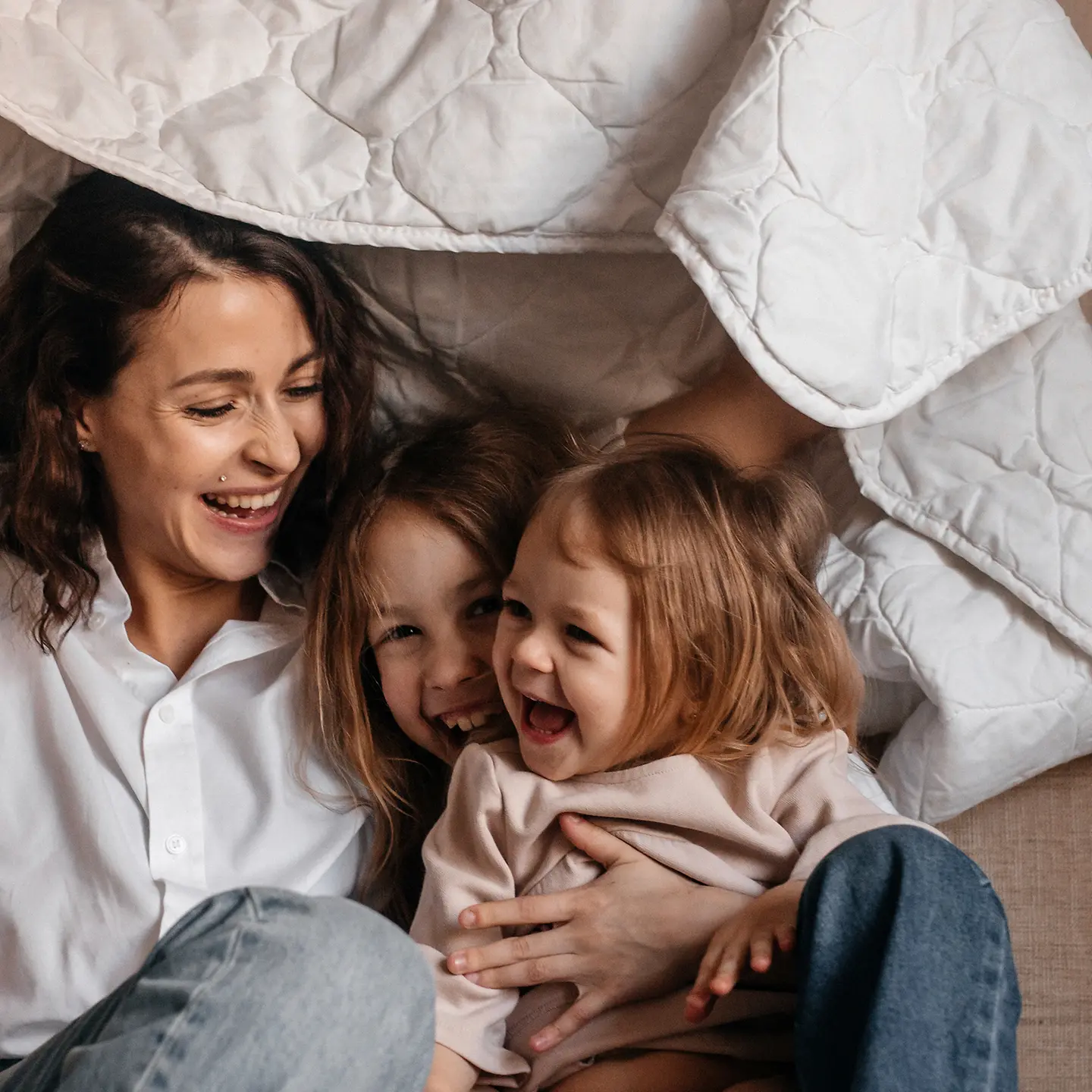 Glückliche Mutter mit drei Mädchen unter einer Decke