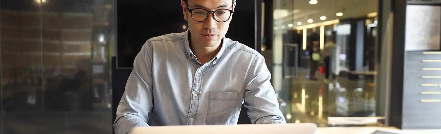 Junger Mann sitzt in modernem Büro am Laptop
