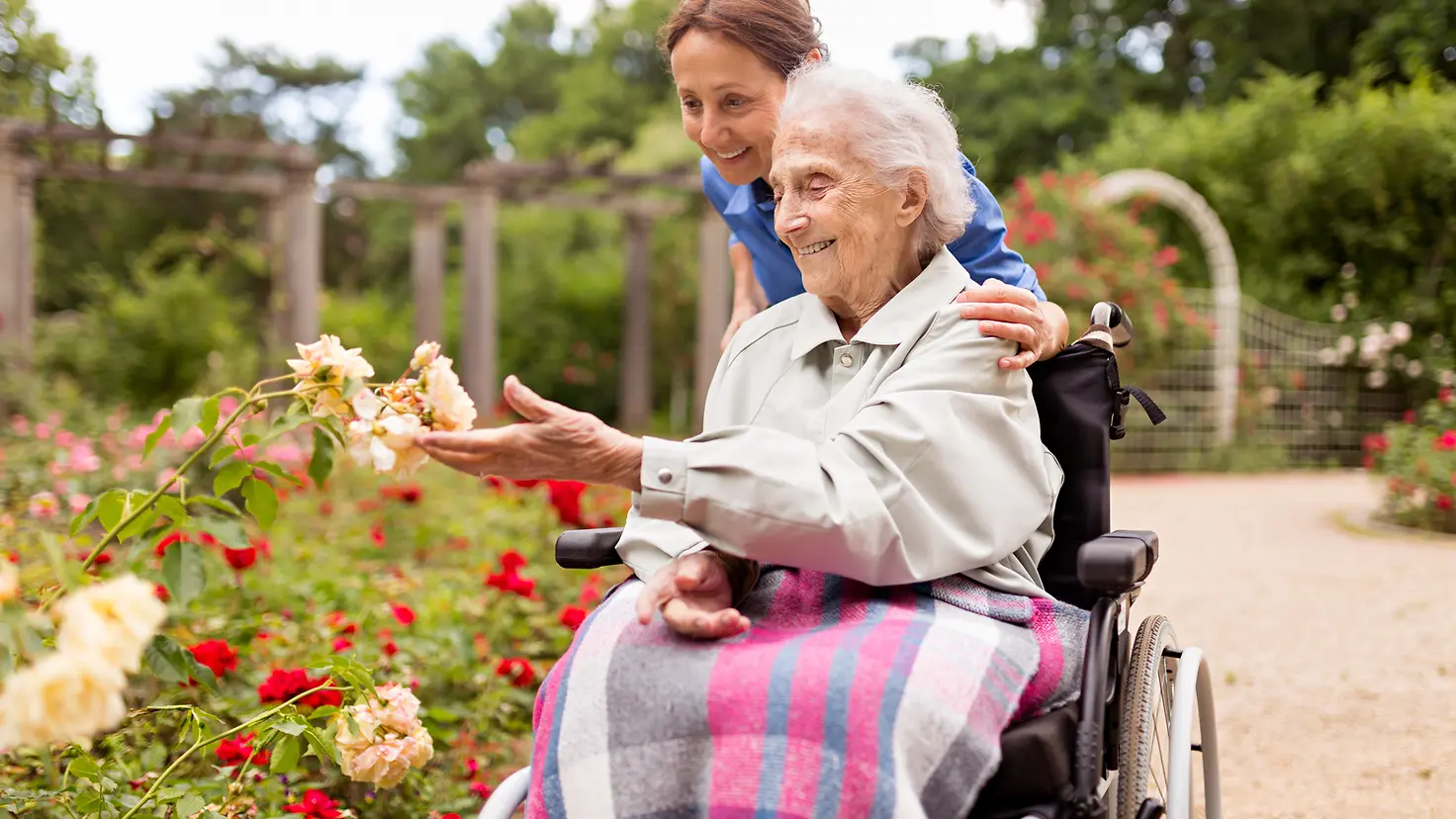 Pflegende Angehörige mit Pflegeperson im Rollstuhl in einem Garten