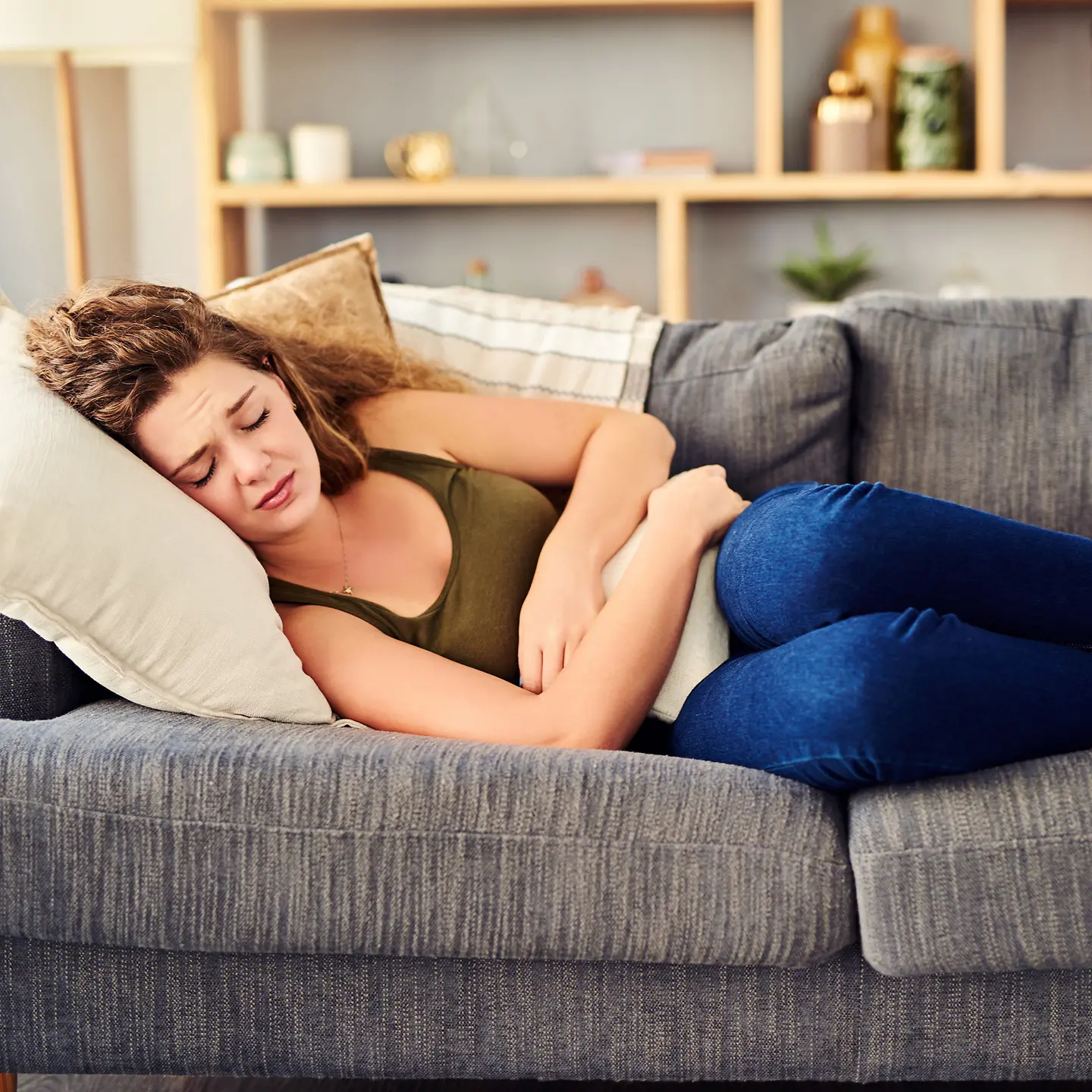 Eine junge Frau liegt mit Endometriose-Schmerzen und einer Wärmflasche auf dem Sofa.