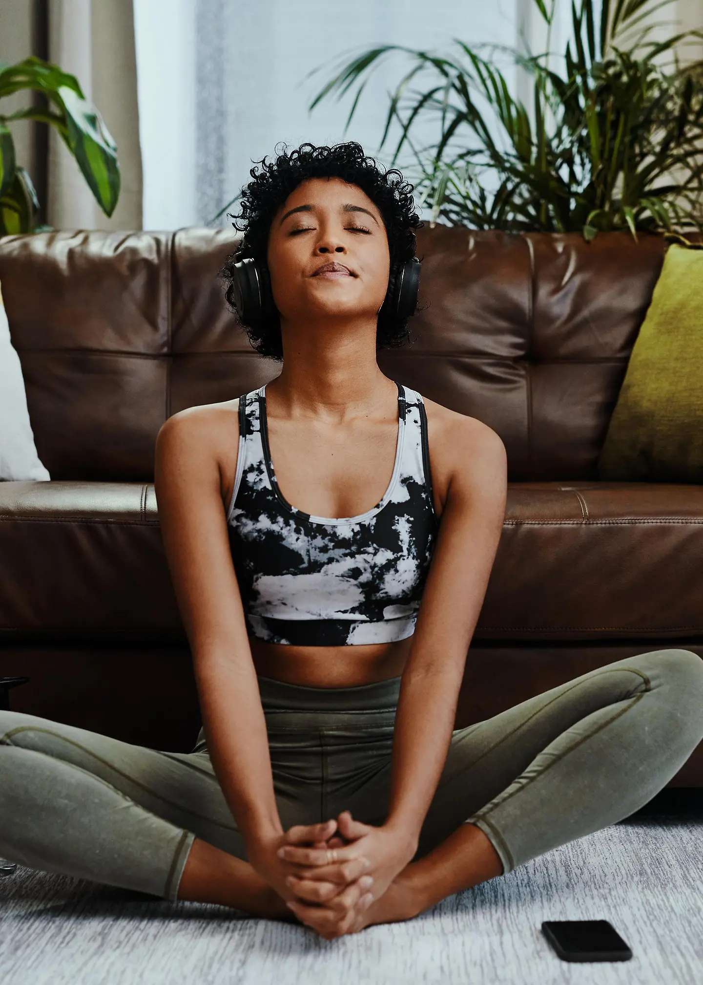 Junge Frau mit Endometriose sitzt mit geschlossenen Augen auf ihrem Teppich und macht Entspannungsübungen