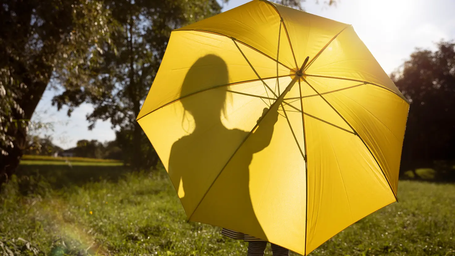 Ein Kind steht hinter einem gelben Schirm in der Sonne