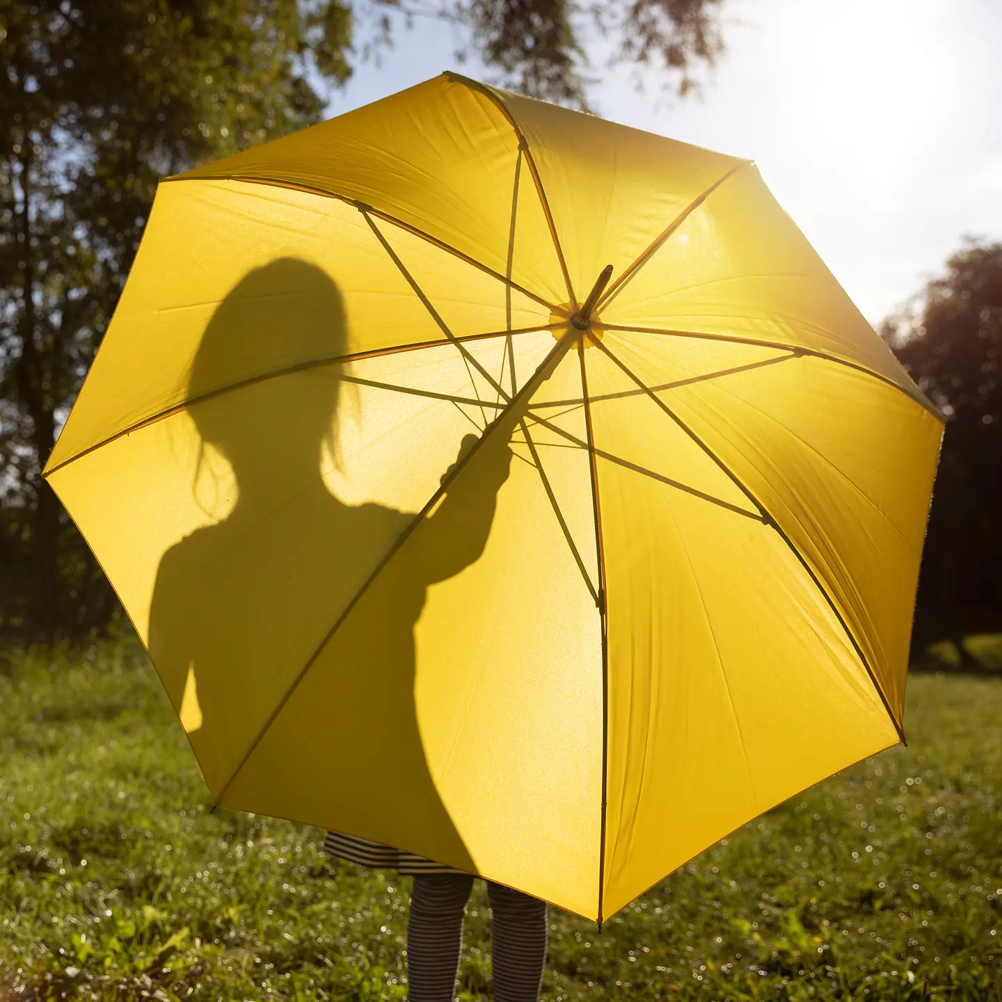 Ein Kind steht hinter einem gelben Schirm in der Sonne
