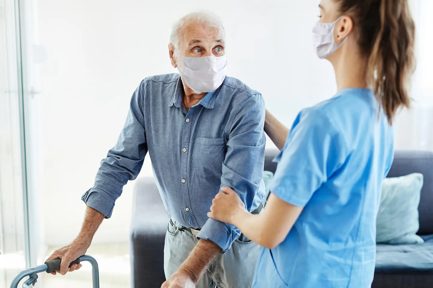 Älterer Mann mit Schutzmaske mit Pflegerin mit Schutzmaske