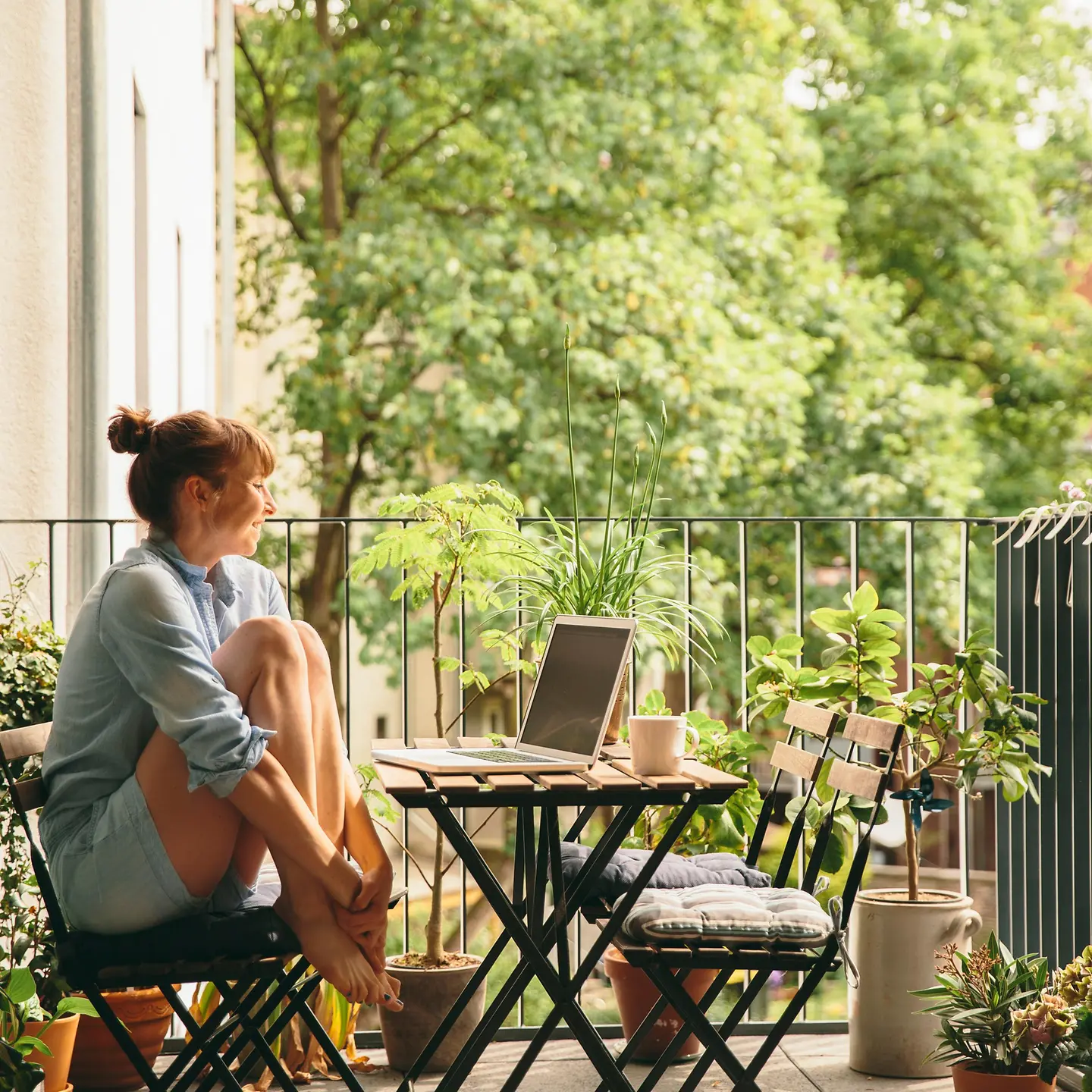 Eine Frau sitzt auf dem Balkon und schaut auf ihren Laptop