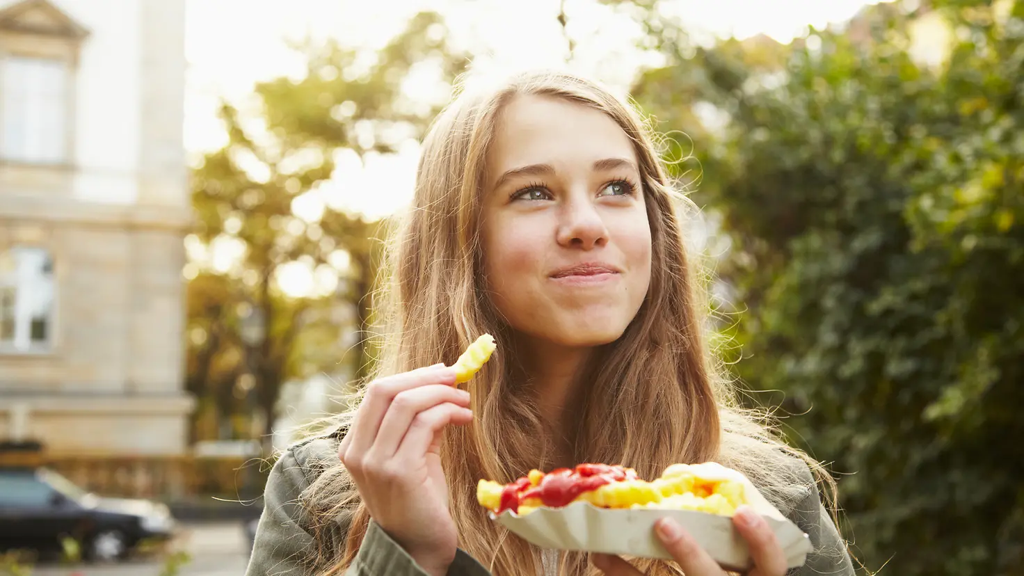 Ein Mädchen isst Pommes Frites mit Tomaten-Ketchup und Mayonnaise. Eine ausgewogene Ernährung wird bei Diabetes Typ 1 empfohlen, wobei nicht auf bestimmte Nahrungsmittel verzichtet werden muss.