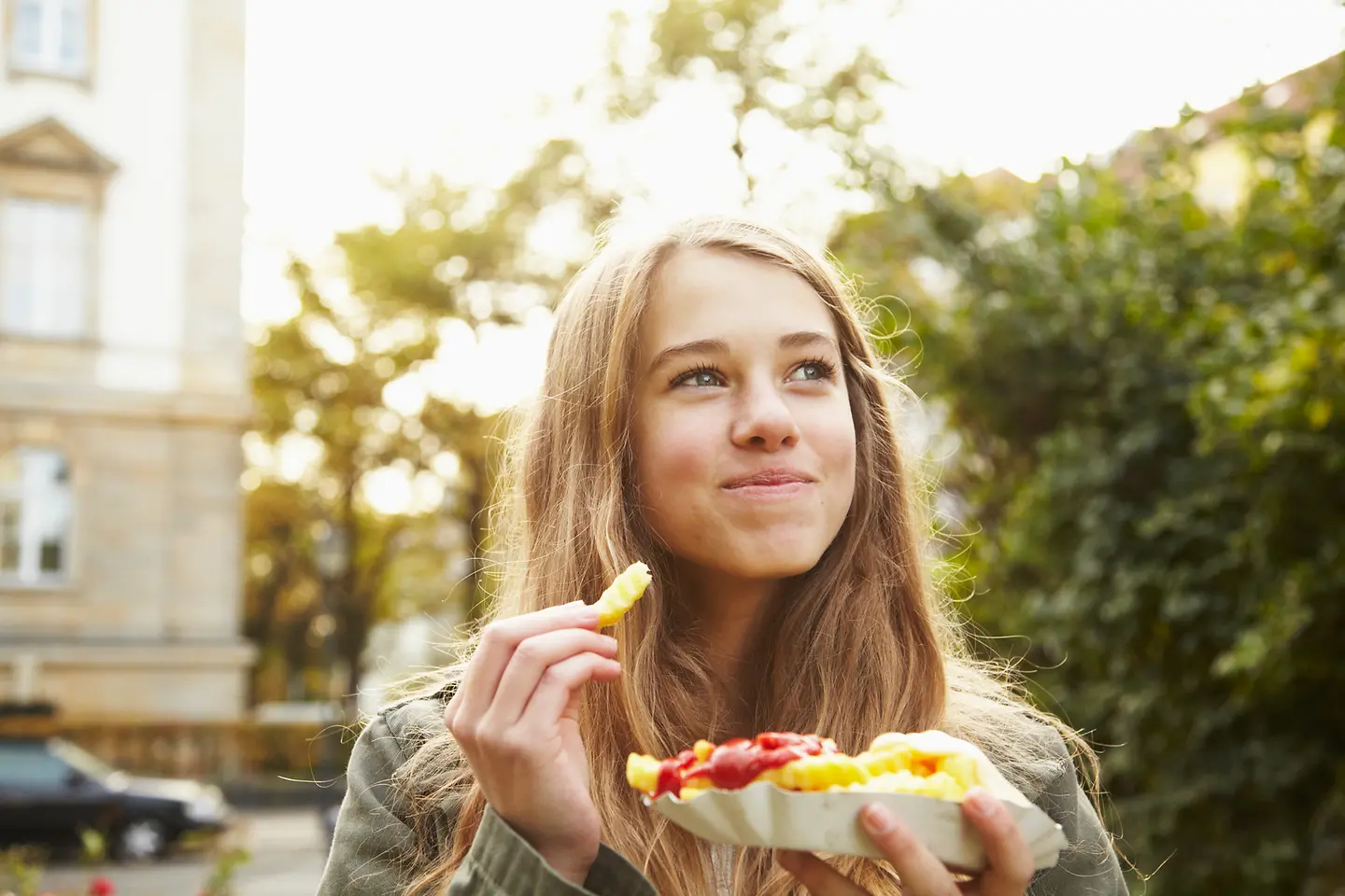Ein Mädchen isst Pommes Frites mit Tomaten-Ketchup und Mayonnaise. Eine ausgewogene Ernährung wird bei Diabetes Typ 1 empfohlen, wobei nicht auf bestimmte Nahrungsmittel verzichtet werden muss.