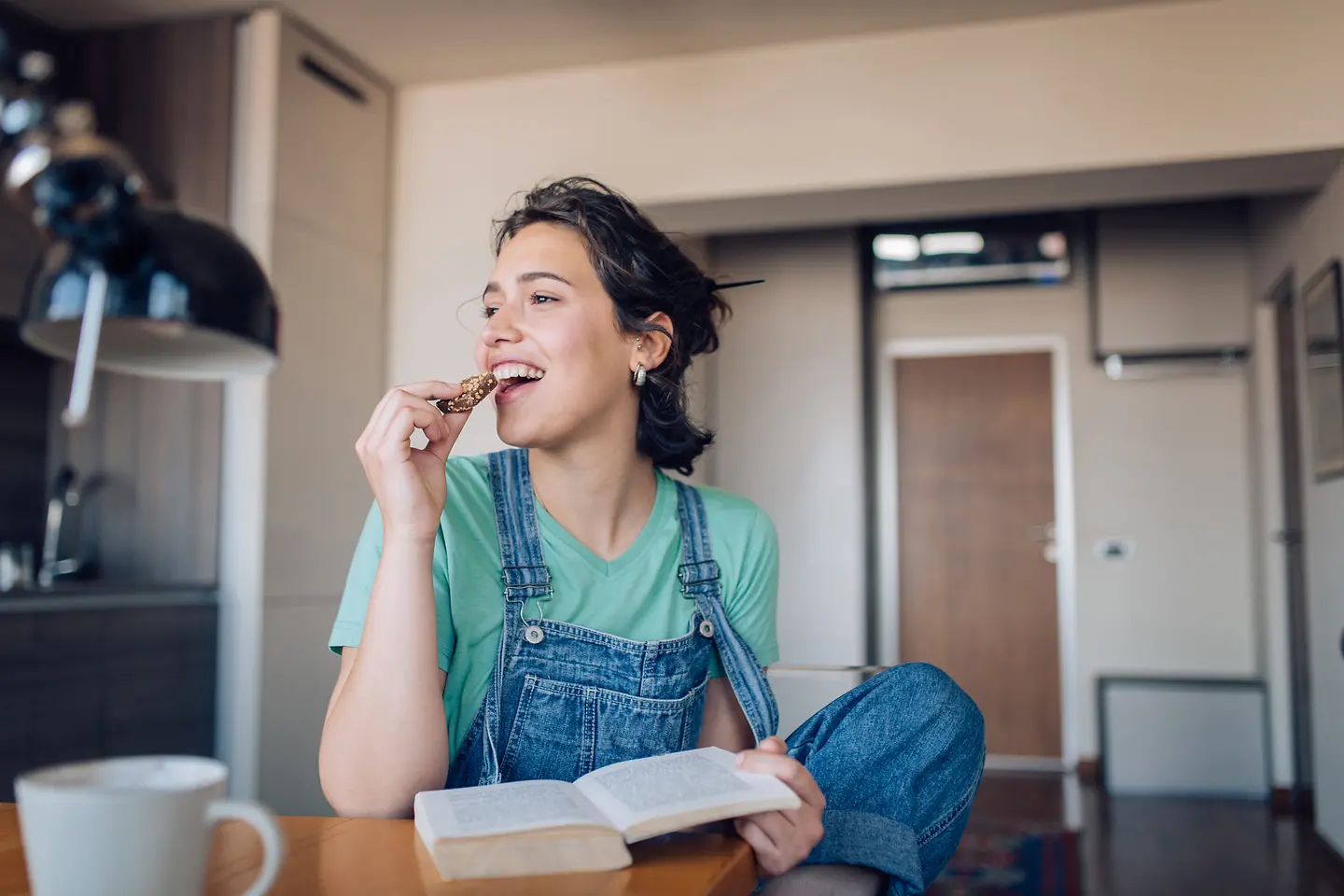 Eine junge Frau isst einen Keks und liest ein Buch. Menschen mit Typ-1-Diabetes müssen keiner strengen Ernährungsform folgen.