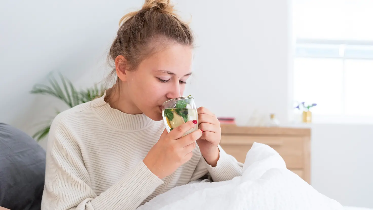Eine junge Frau sitzt im Bett und trinkt eine Tasse Tee. 