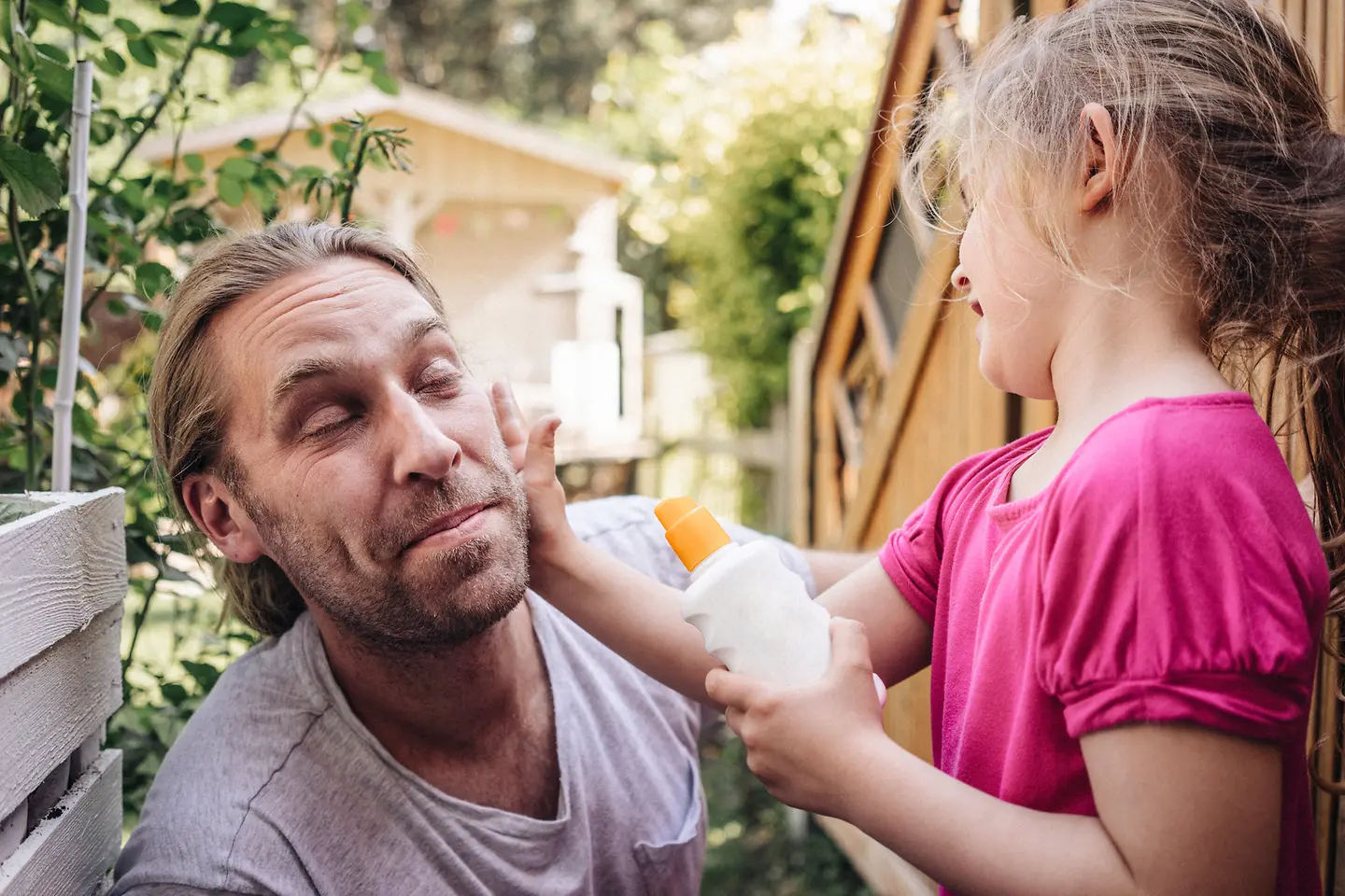 Ein Mädchen cremt ihren Vater im Gesicht mit Sonnencreme ein, um ihn vor weißem Hautkrebs zu schützen. 