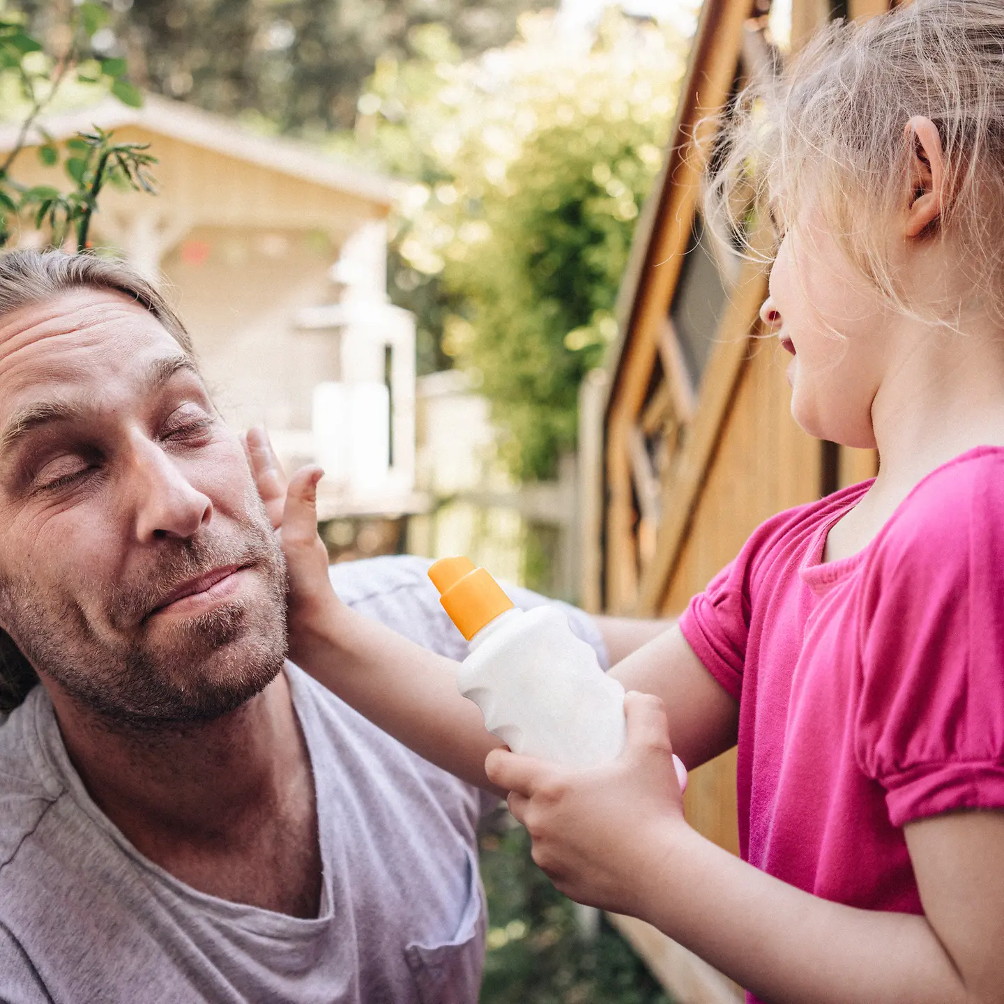 Ein Mädchen cremt ihren Vater im Gesicht mit Sonnencreme ein, um ihn vor weißem Hautkrebs zu schützen. 