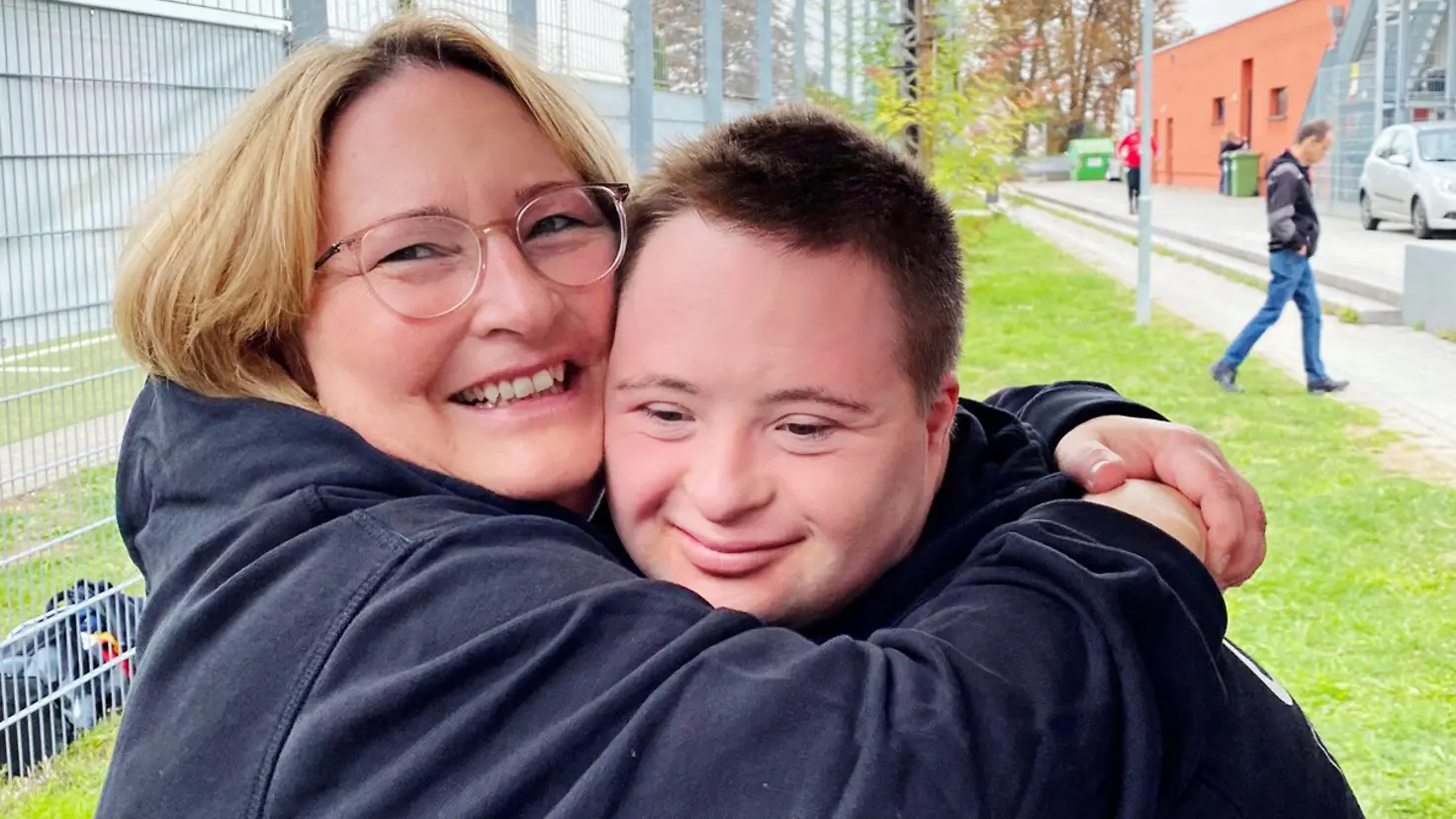 Eine Frau mit Brille umarmt ihren Sohn.