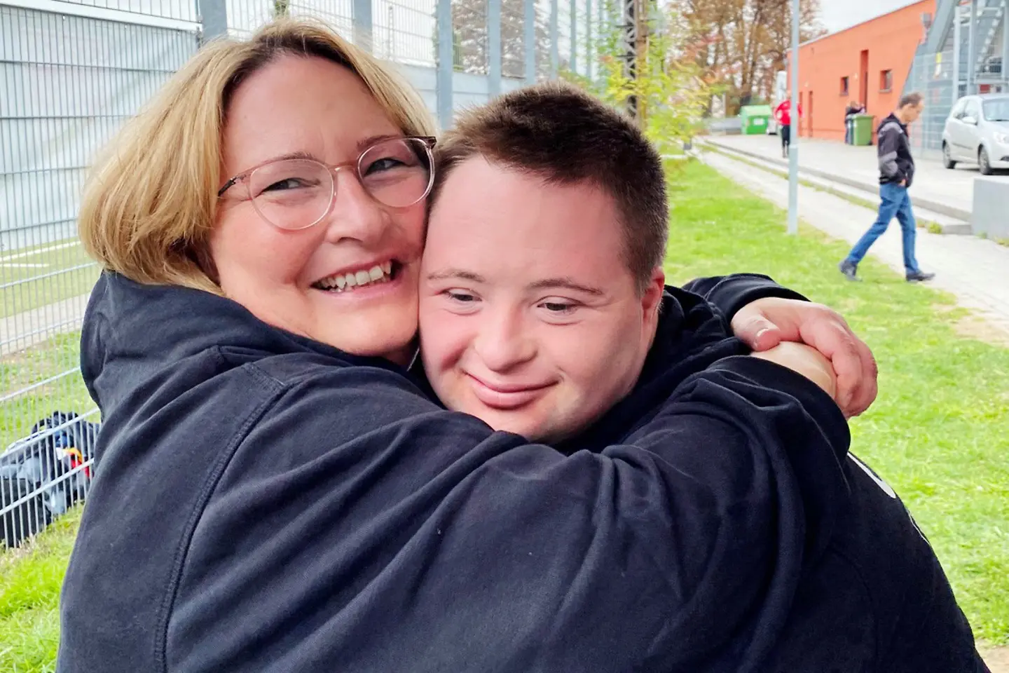 Eine Frau mit Brille umarmt ihren Sohn.