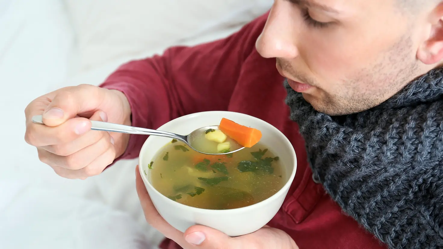 Ein Mann mit Schaal um den Hals isst eine warme Suppe