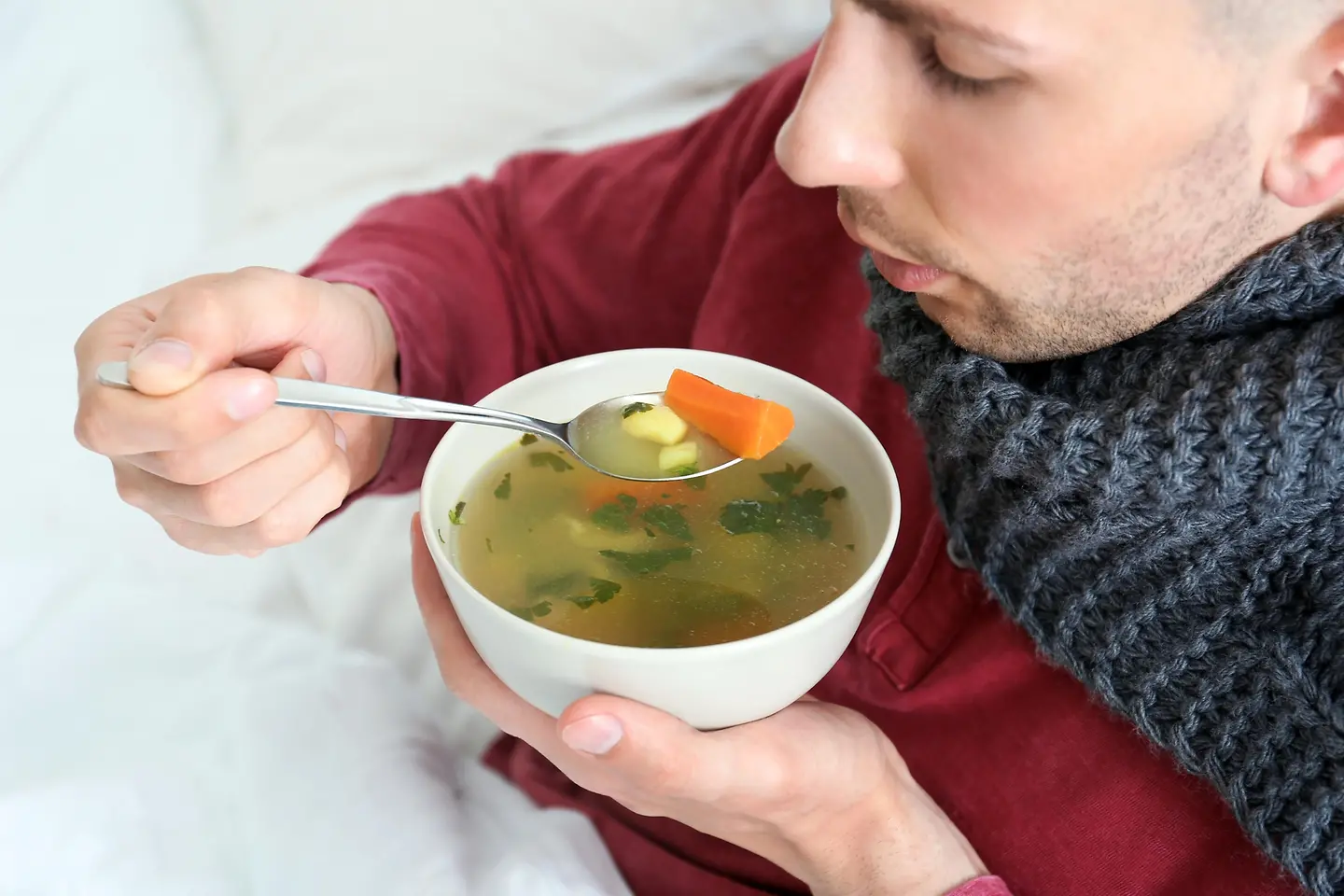 Ein Mann mit Schaal um den Hals isst eine warme Suppe