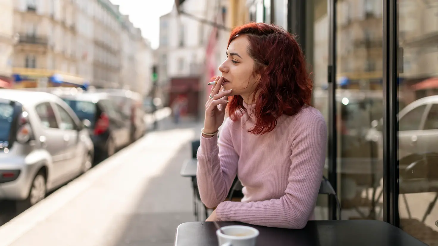 Eine Frau sitzt rauchend in einem Straßencafe.