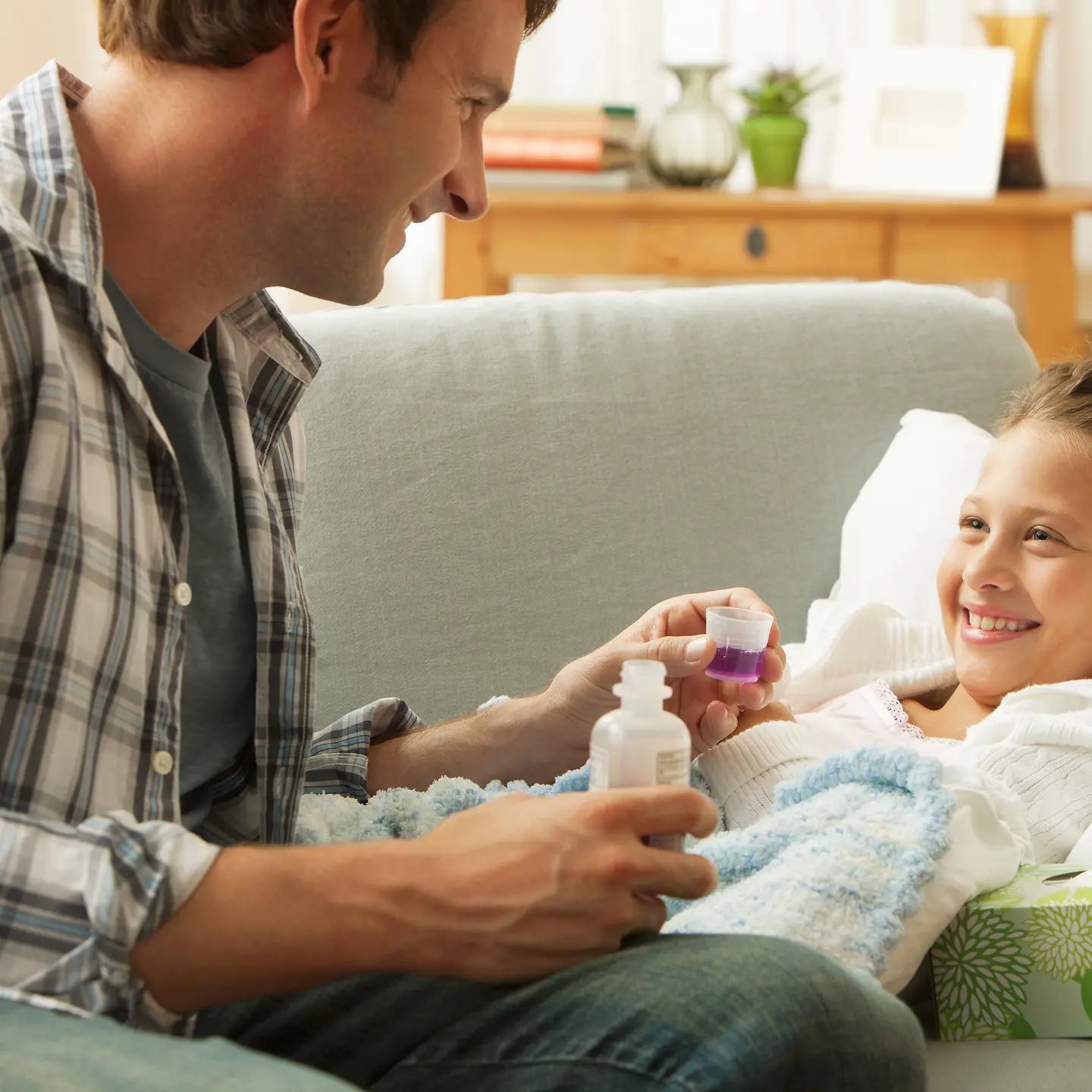 Ein Vater kann dank Kinderkrankenschein seine kranke Tochter pflegen und gibt ihr Medikamente.