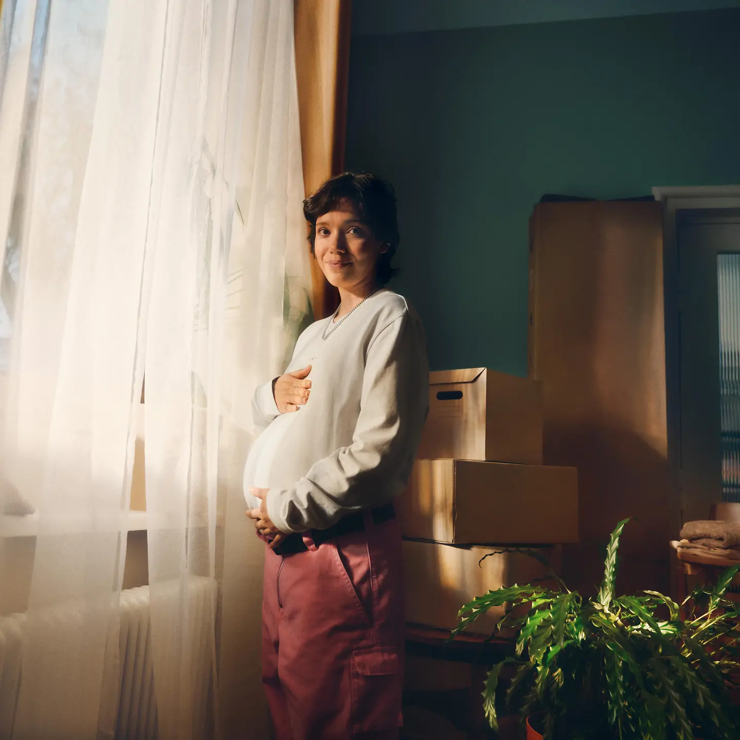 Eine schwangere Frau steht vor einem Fenster