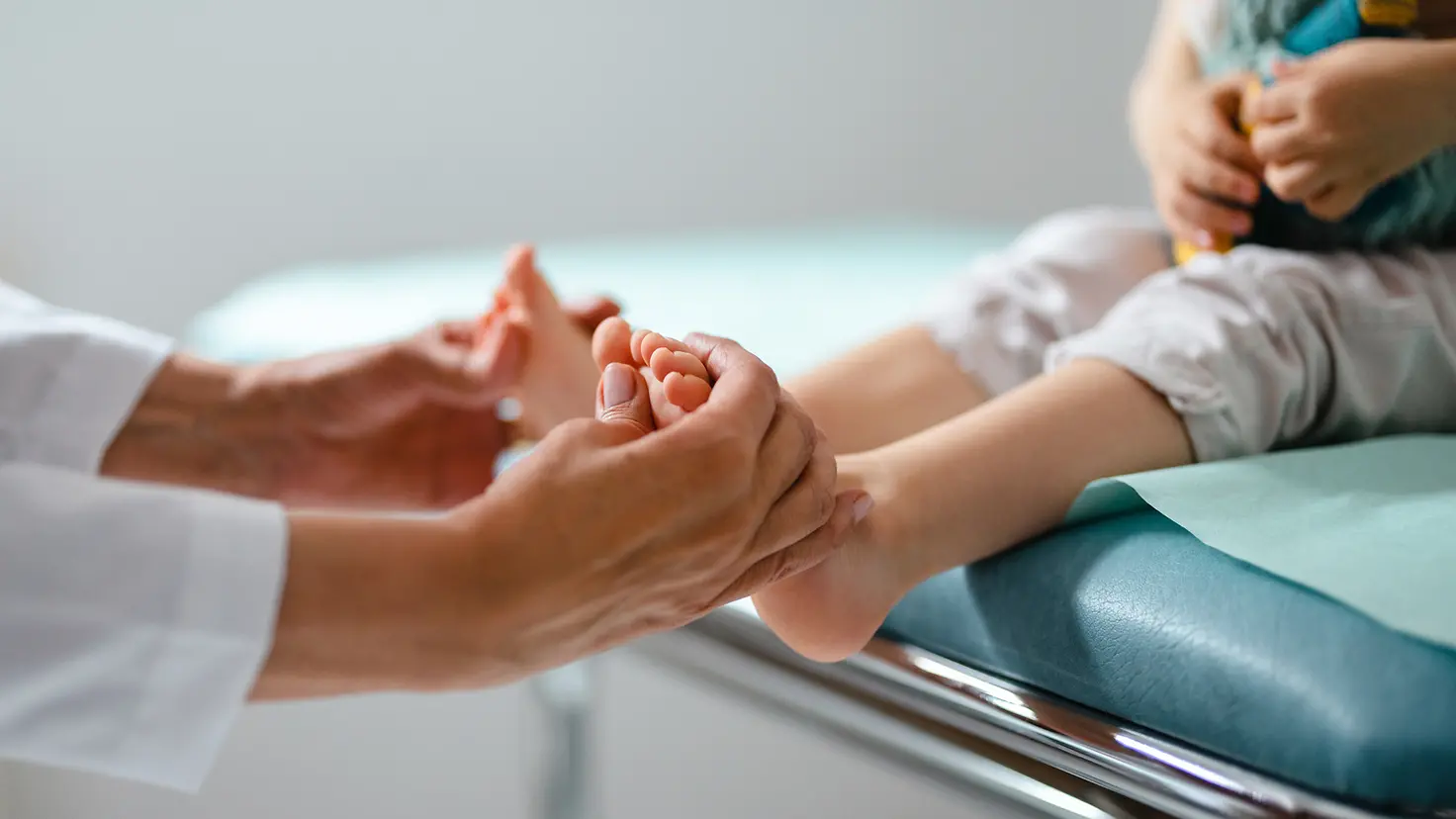 Die Hände einer Ärztin untersuchen die Füße eines Kindes auf Symptome einer Neuropathie.