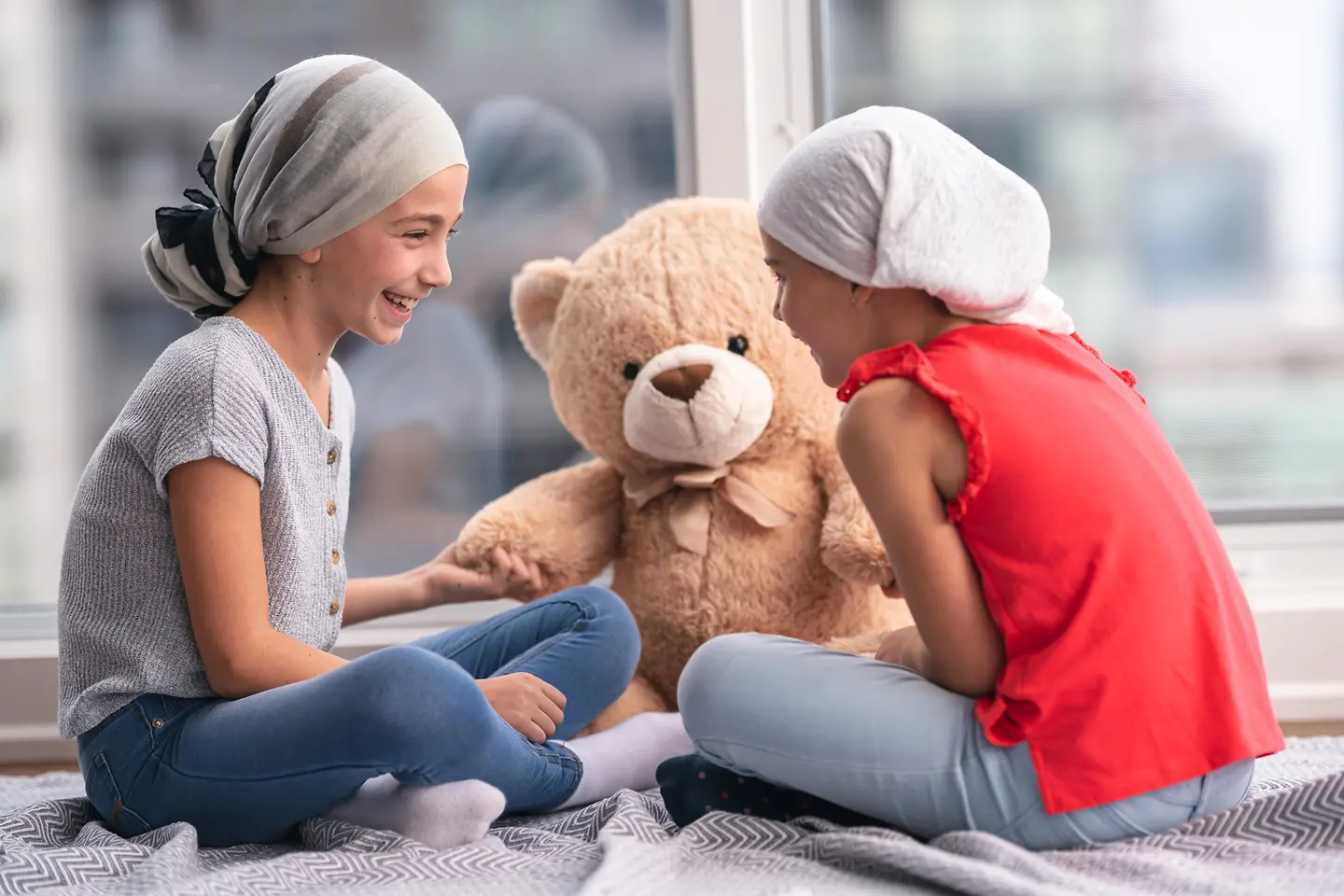 Zwei junge Patientinnen mit Leukämie lachen miteinander.