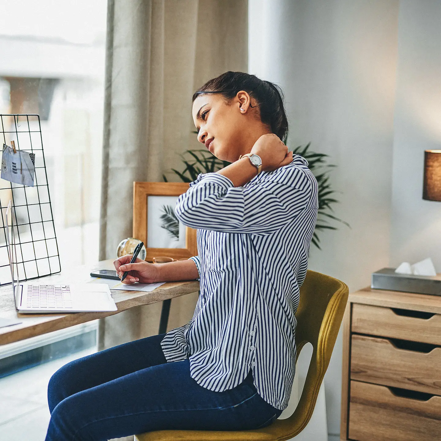 Frau mit Rückenschmerzen sitzt am Schreibtisch.