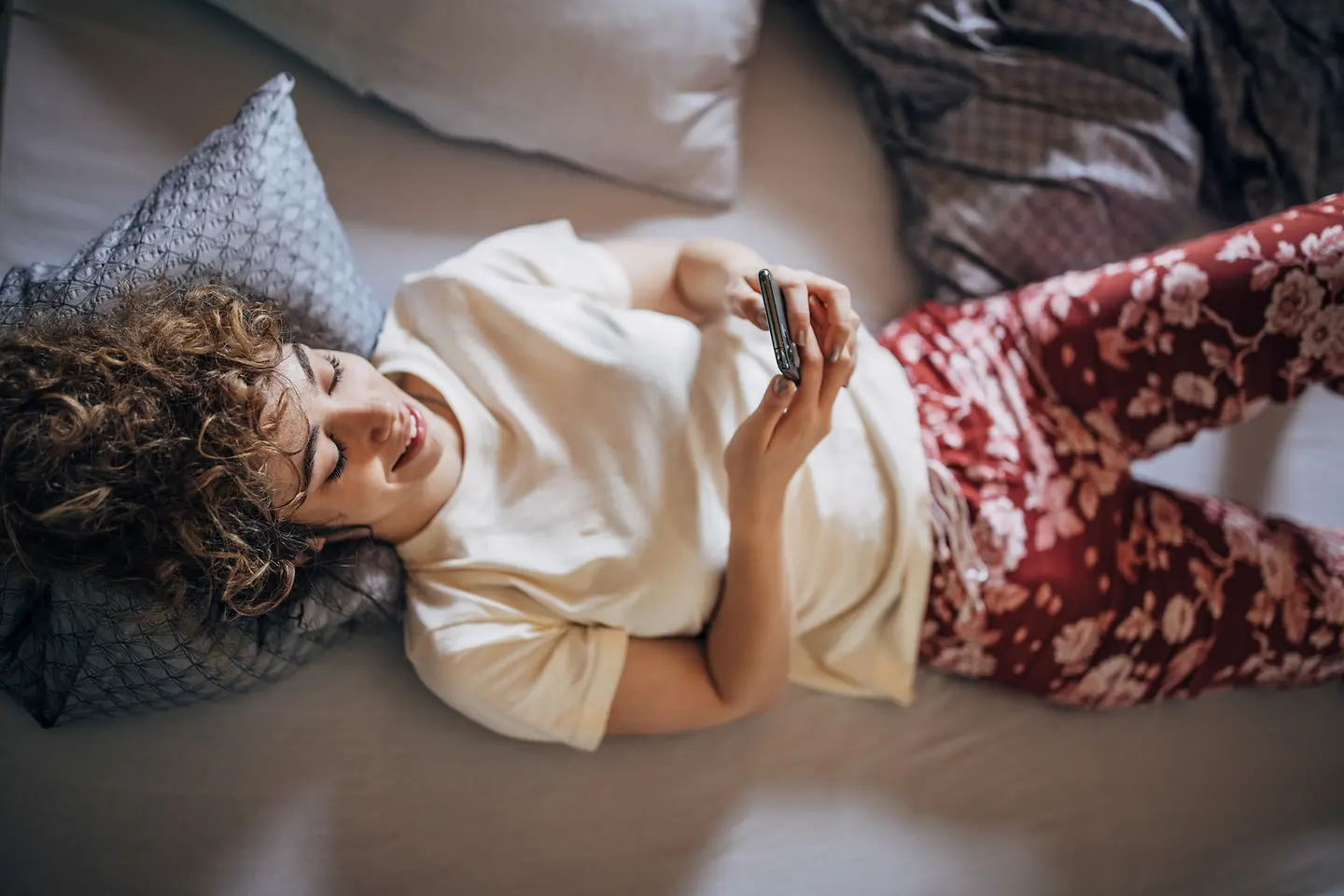 Eine junge Frau im Bett verfolgt über die Barmer-App auf ihrem Mobiltelefon den Status ihrer Krankmeldung.