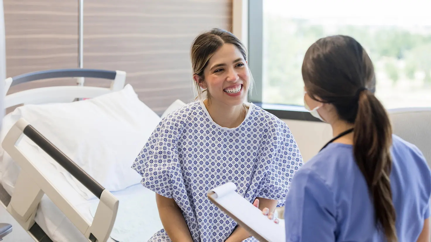 Eine junge Frau im Krankenhaus spricht lächelnd mit einer Ärztin.