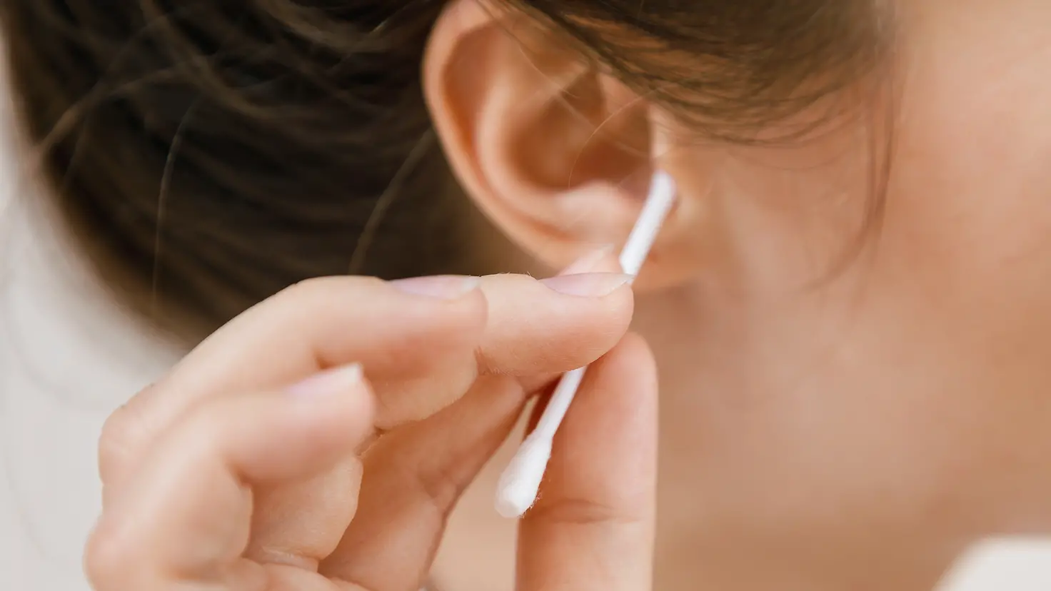Rechtes Ohr einer jungen Frau, die mit einem Wattestäbchen versucht, ihr Ohr zu reinigen.