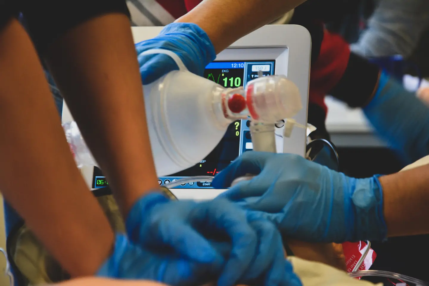Zu sehen sind die Hände von zwei Menschen in blauen Latexhandschuhen, die einen Körper künstlich beatmen und eine Herzdruckmassage durchführen