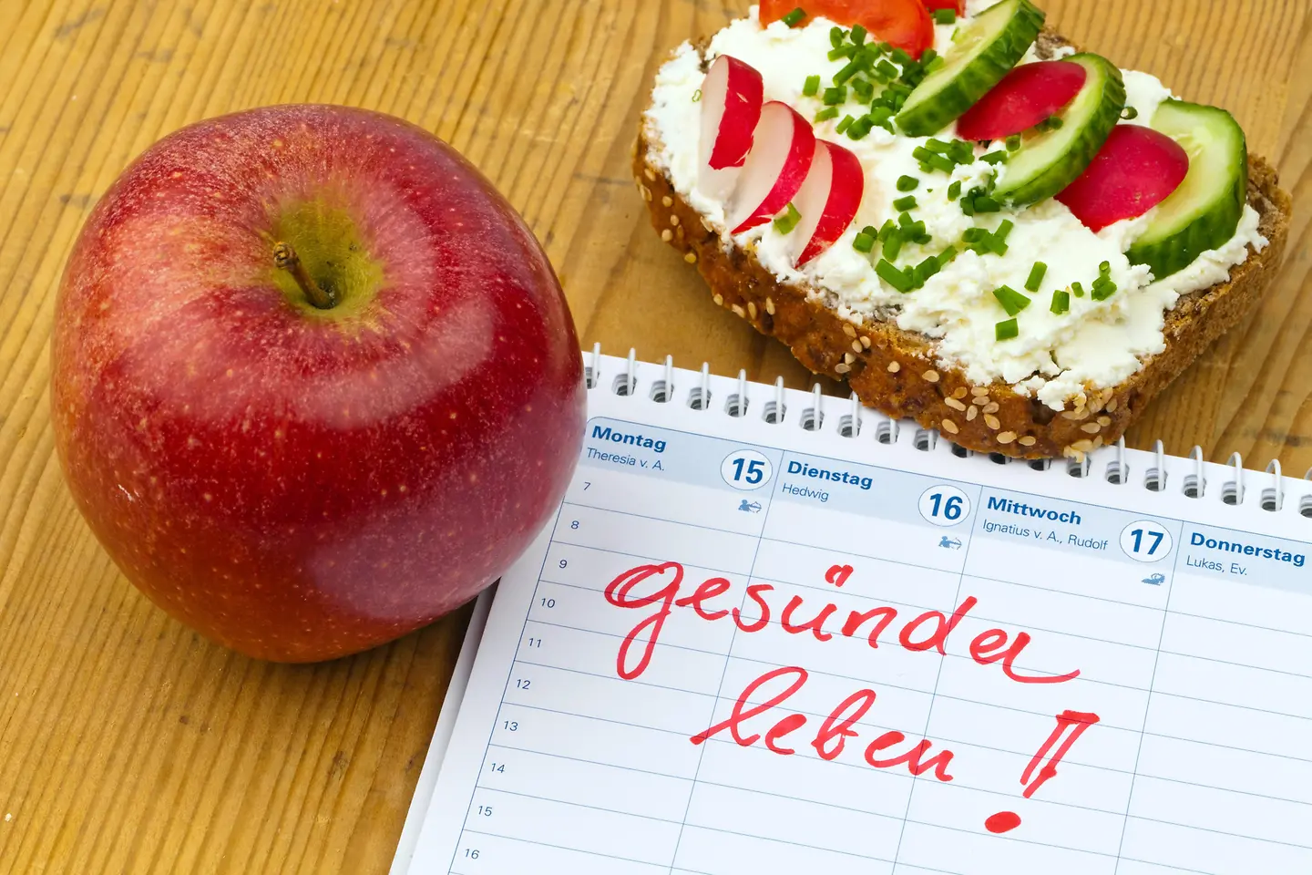 Zu sehen ist die Notiz "Gesünder leben!", daneben ein Apfel und ein Vollkornbrot mit Frischkäse 