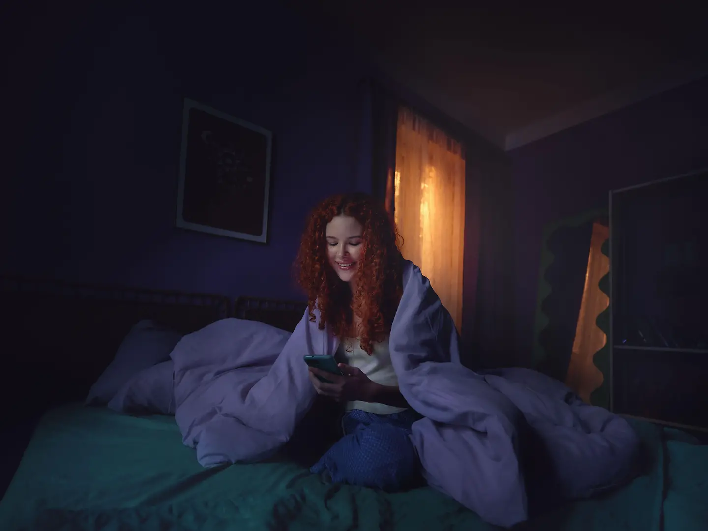 Eine Frau sitzt auf dem Bett und schaut auf ihr Handy.