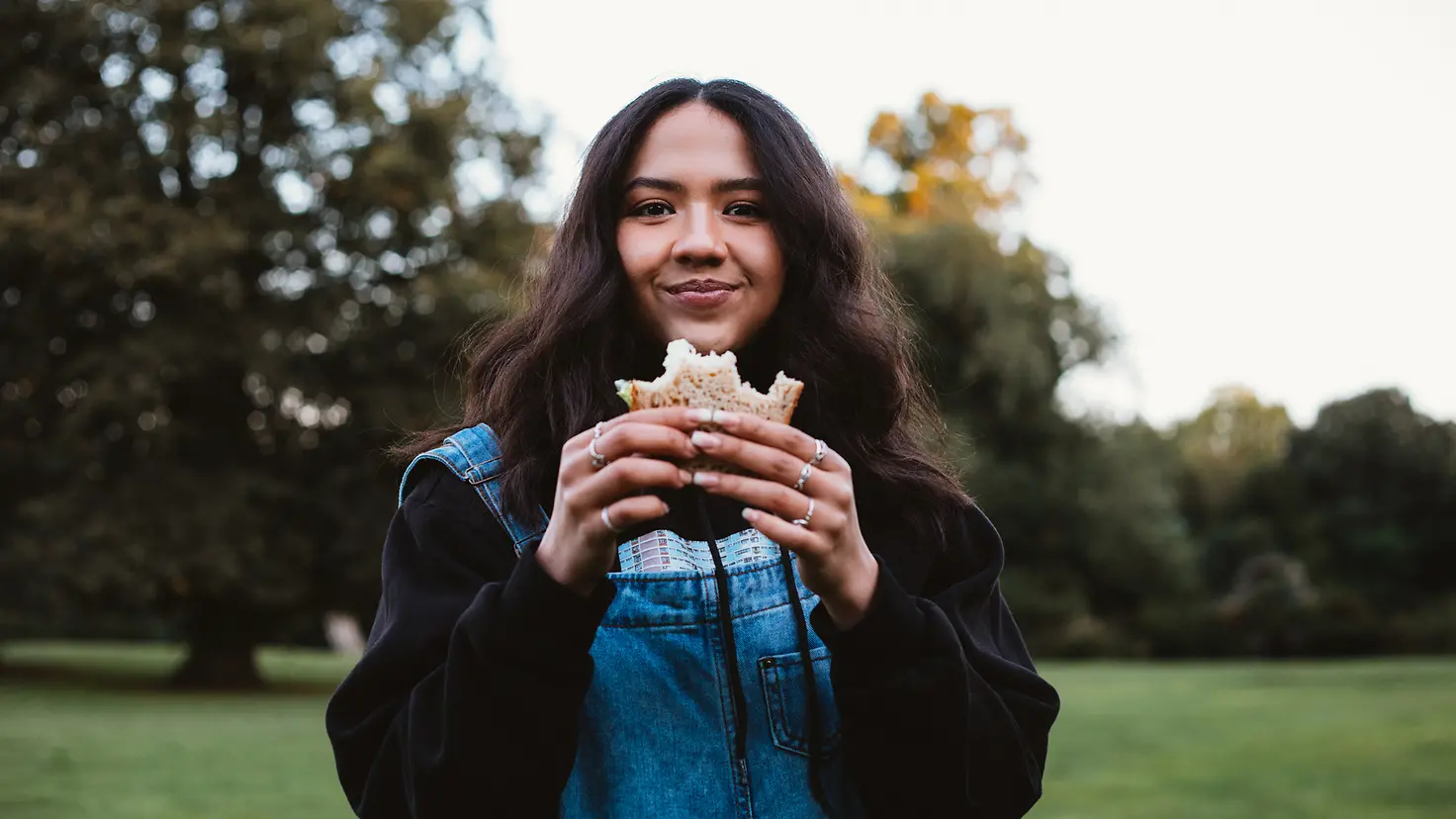 Eine junge Frau isst ein belegtes Brot im Park.