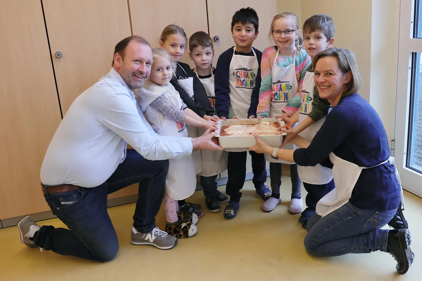 Kita-Kinder, ein BARMER-Mitarbeiter und die Genussbotschafterin halten eine Schüssel mit Linsen-Lasagne in der Hand.