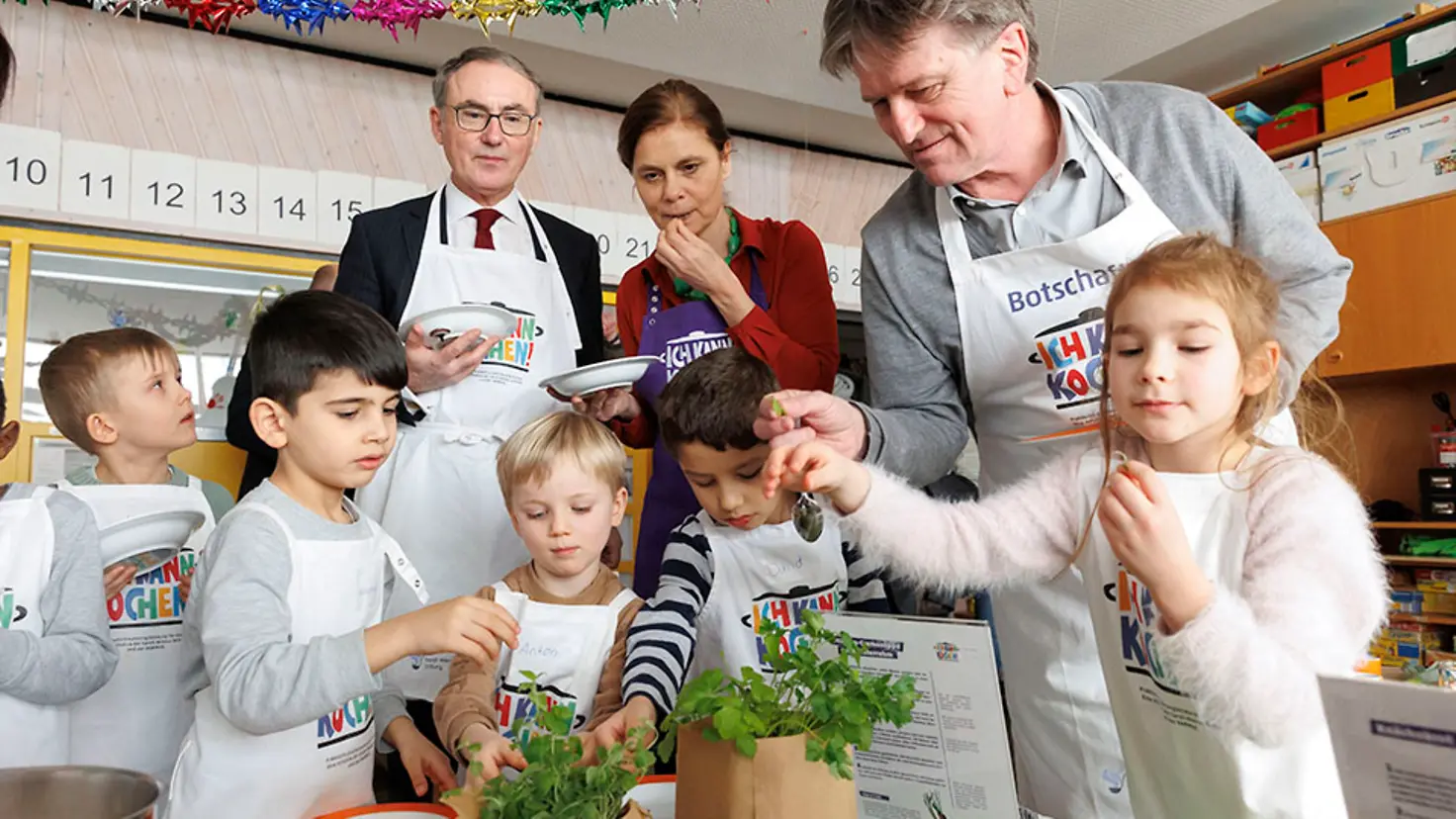 Zwei Männer und eine Frau probieren mit fünf Kindern frische Kräuter.