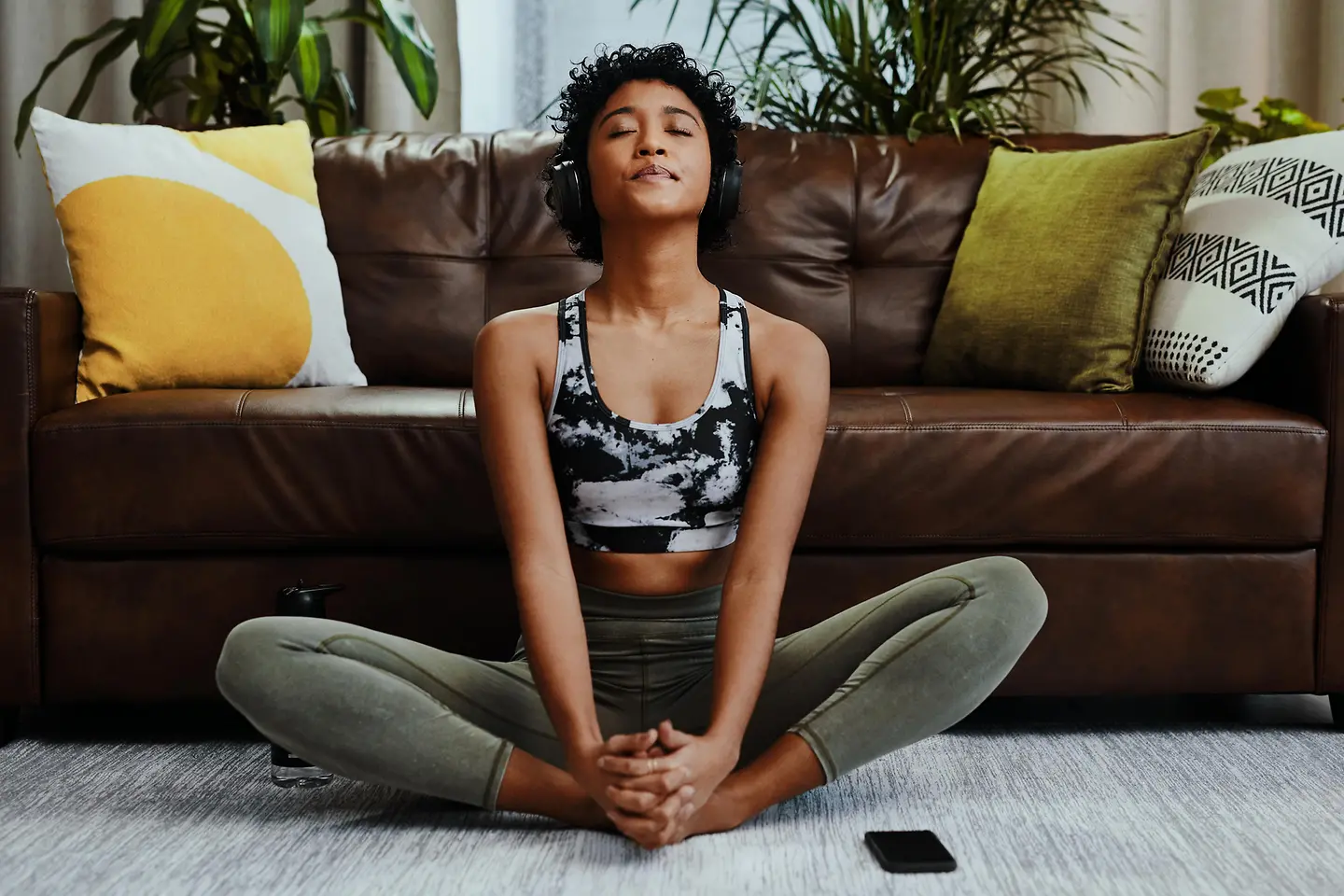 Junge Frau mit Fibromyalgie sitzt mit geschlossenen Augen auf ihrem Teppich und macht sanfte Sportübungen