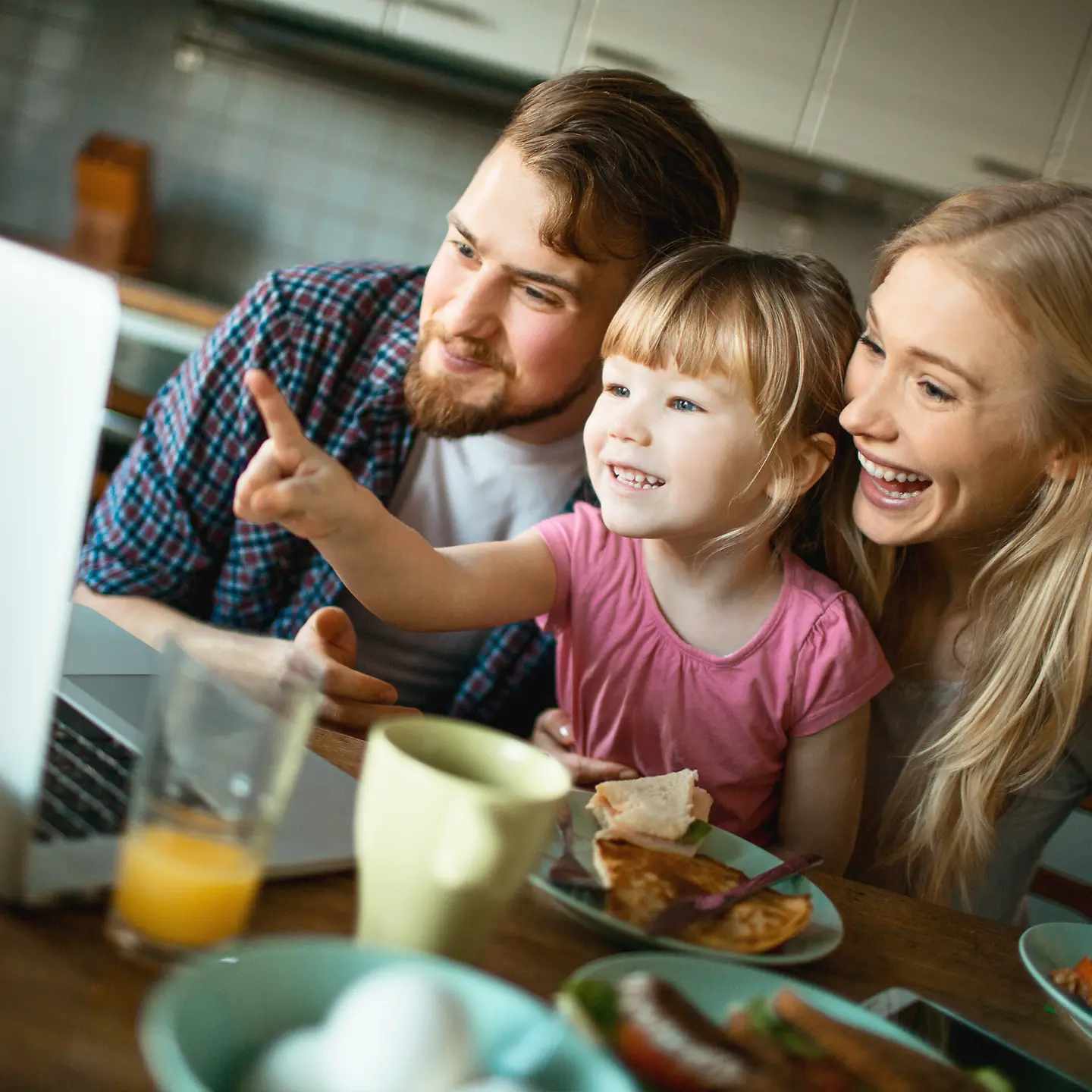 Eine Familie sitzt am Frühstückstisch und betrachtet den Gesundheitsmanager am Laptop