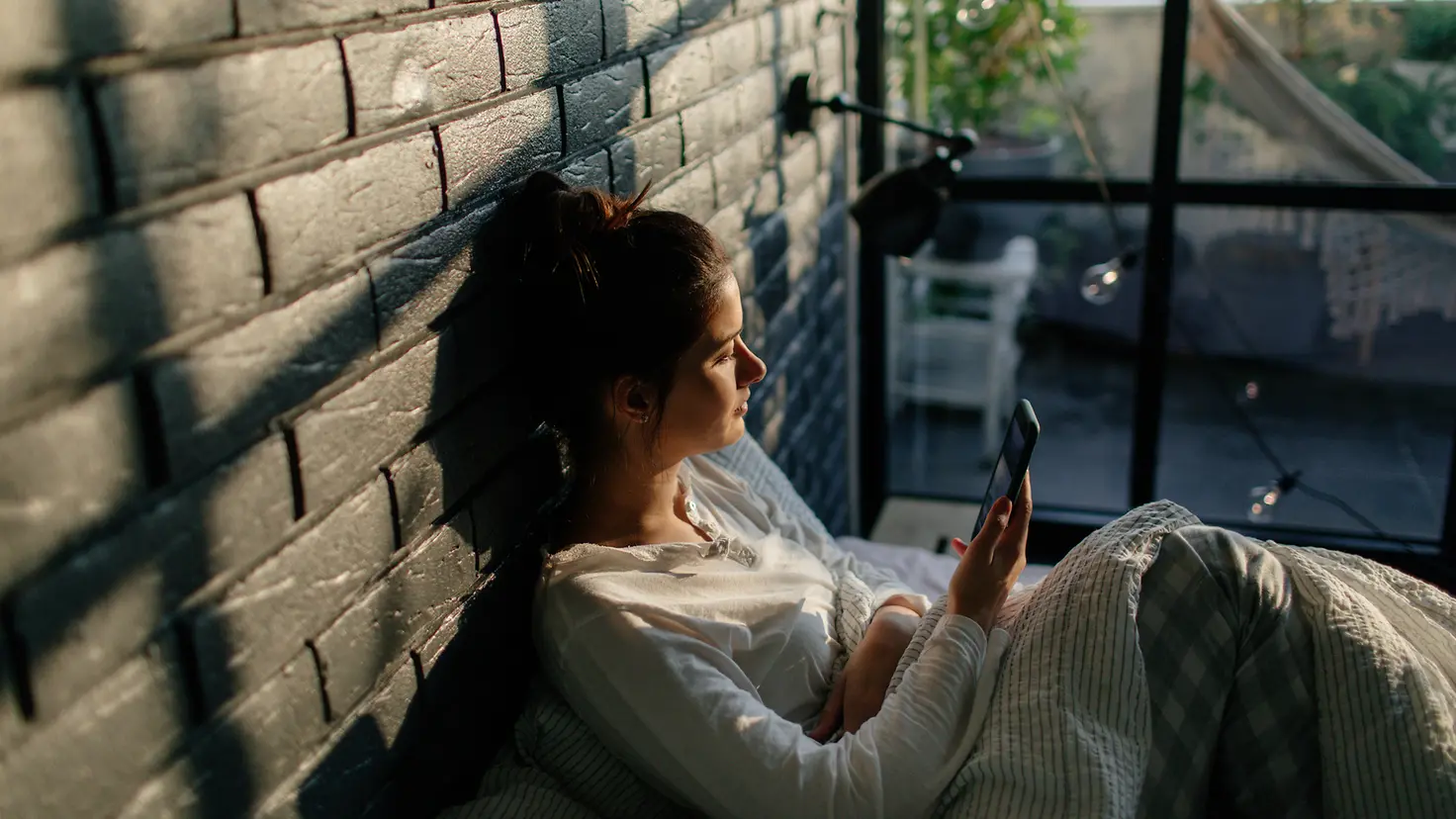 Junge Frau sitzt in einem Wintergarten und schaut auf ihr Handy
