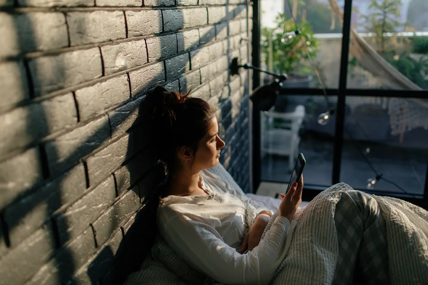 Junge Frau sitzt in einem Wintergarten und schaut auf ihr Handy