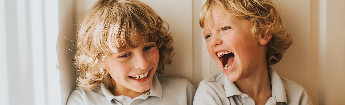 Zwei Kinder lehnen an einer Wand und lachen
