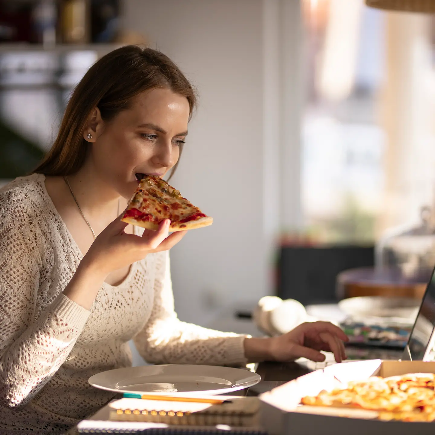 Eine junge Frau sitzt vor dem Computer und isst Pizza.