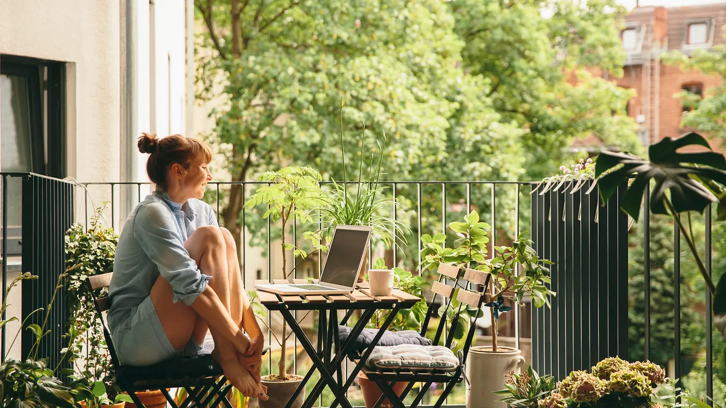 Eine Frau sitzt auf dem Balkon und schaut auf ihren Laptop