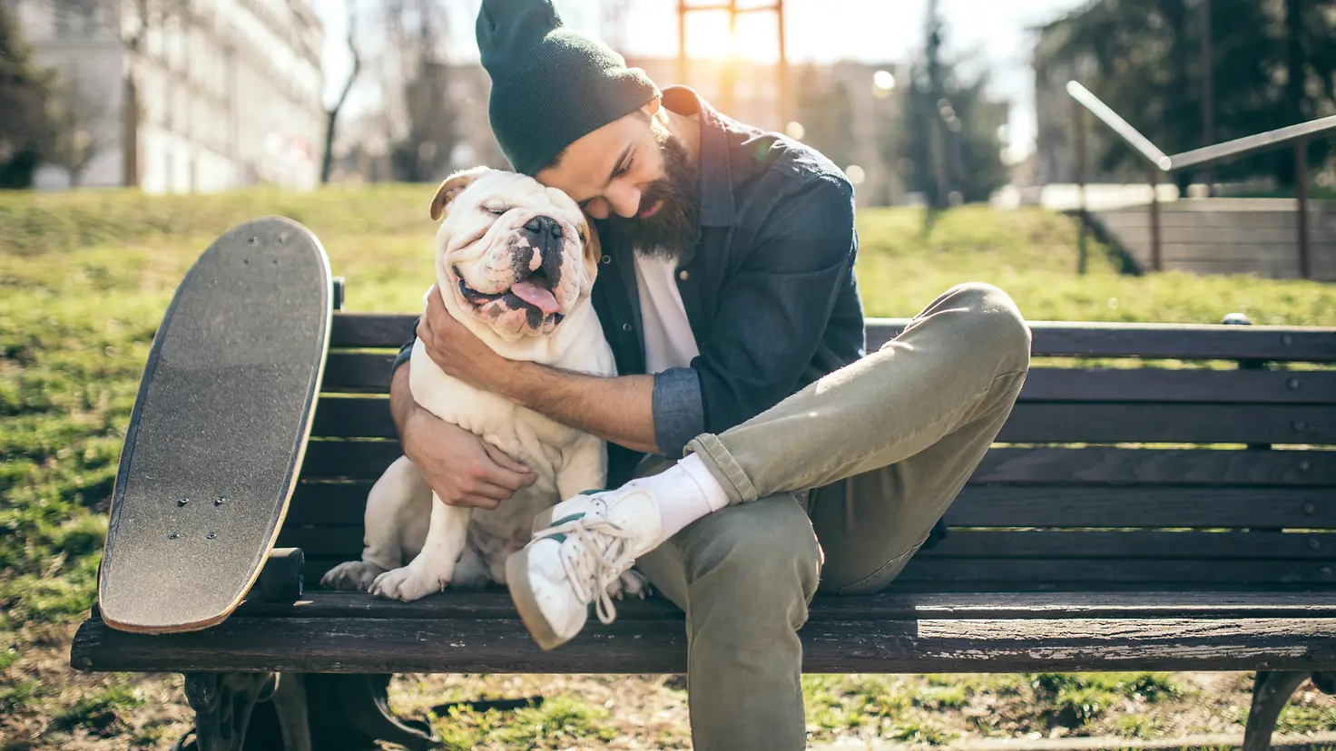 Ein Mann umarmt seinen Hund auf einer Bank